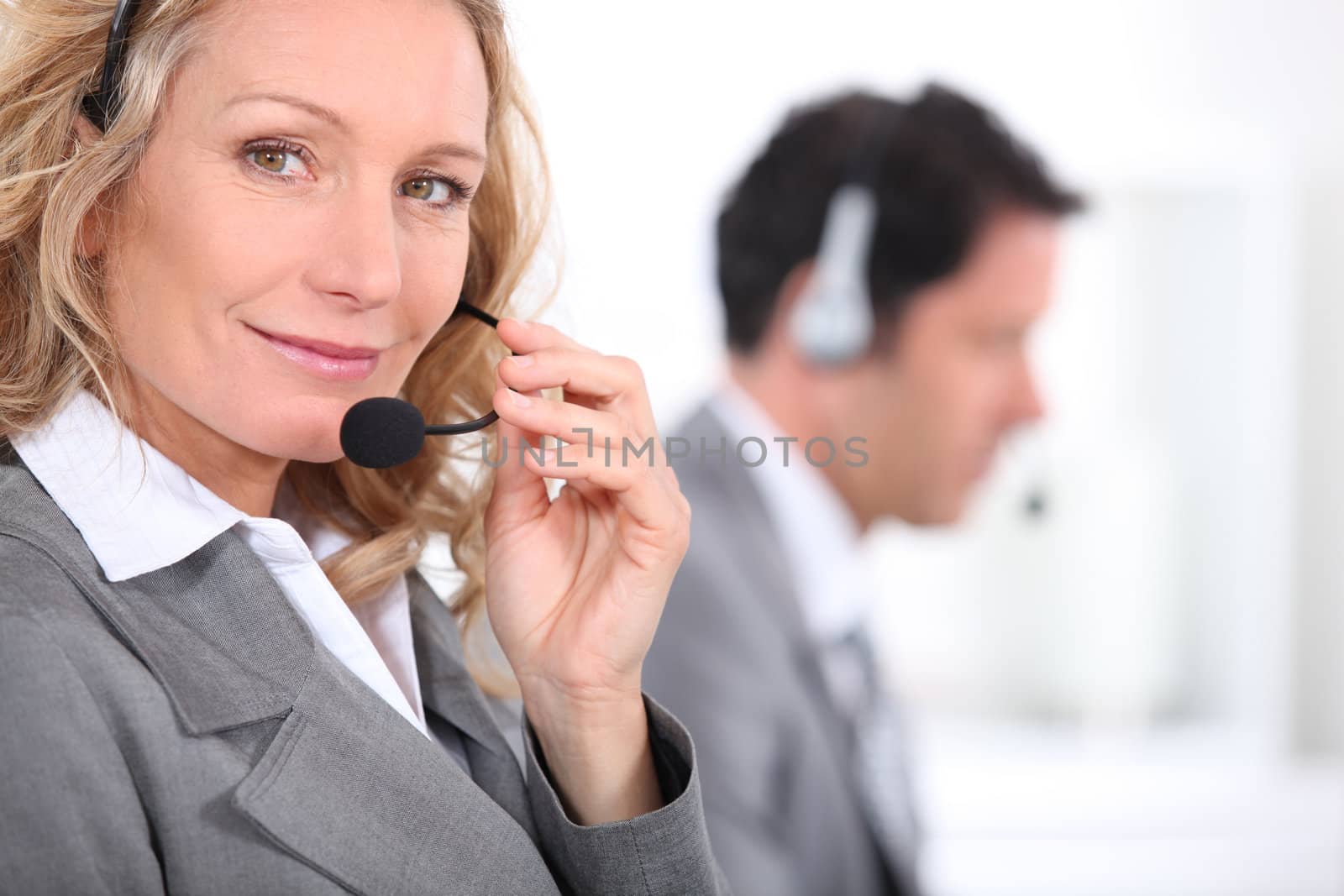 Woman in a suit using a headset with a male colleague in the background