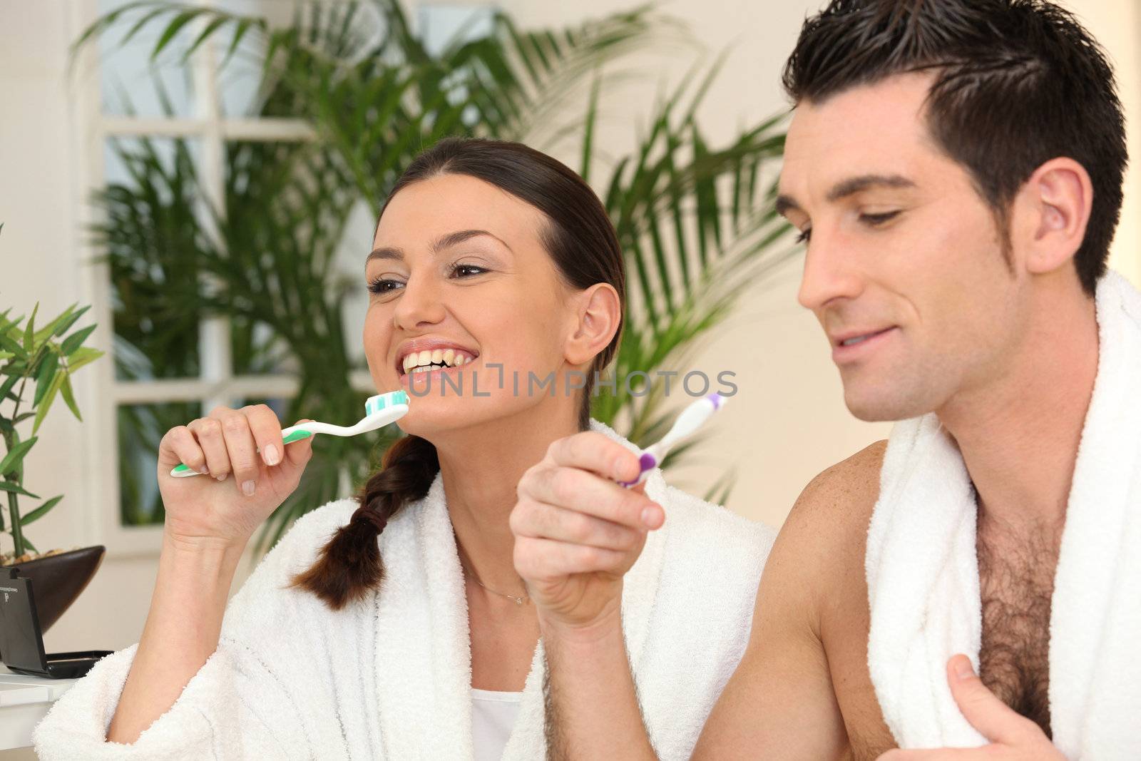 Couple brushing teeth in bathroom by phovoir