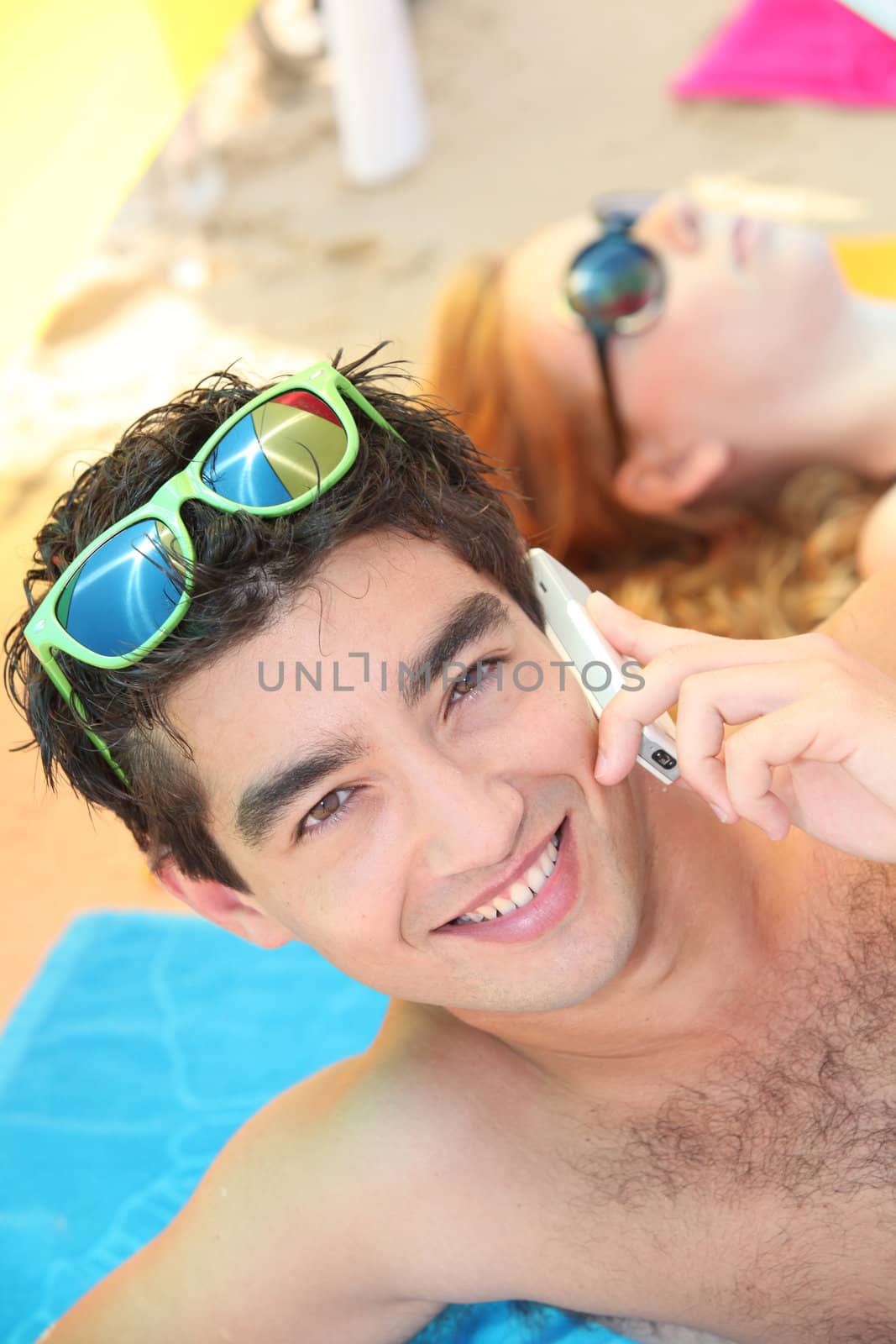 man lying on a beach, using his phone