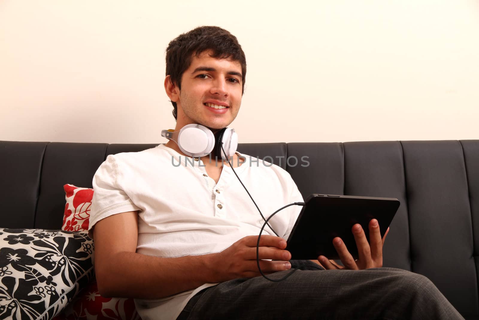 A young, latin man with a Tablet PC and Headphones on the Sofa