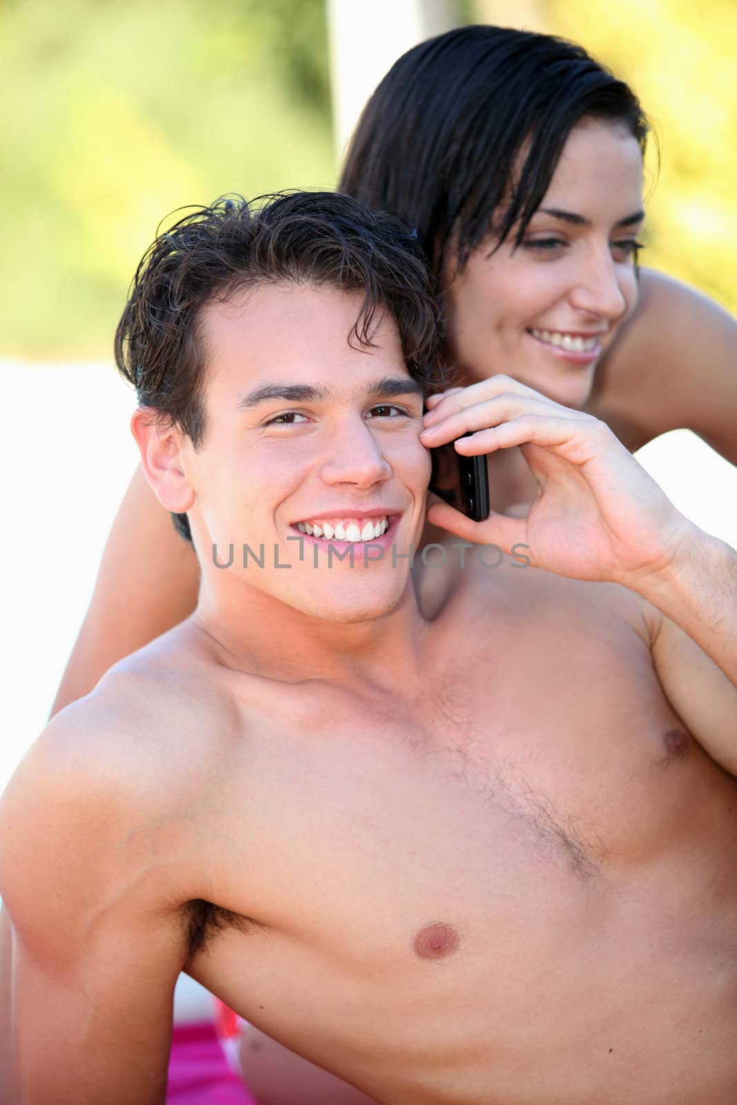 bare-chested boy phoning with girlfriend by his side by phovoir