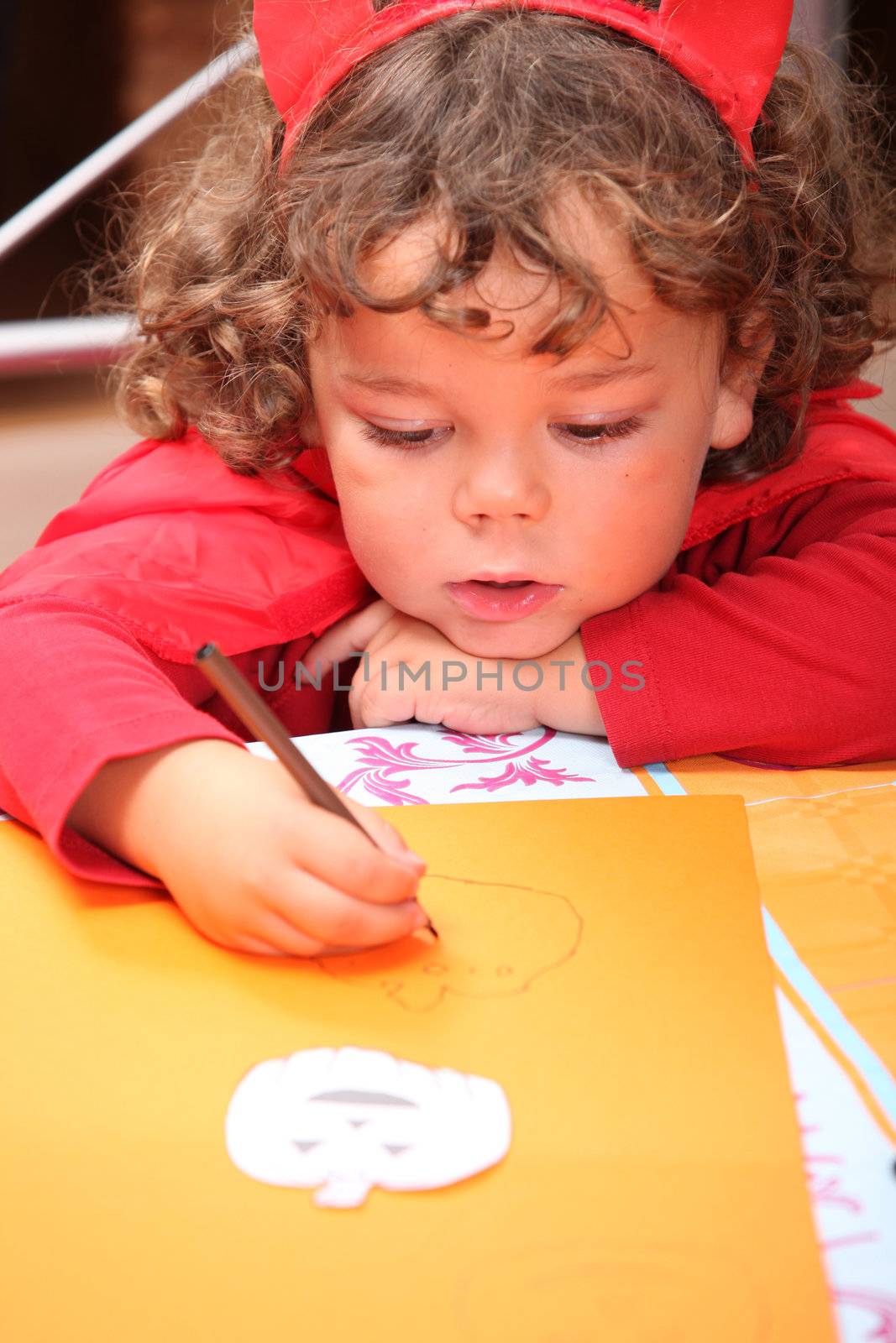 Closeup of a child in a red devil's outfit drawing jack-o-lanterns by phovoir