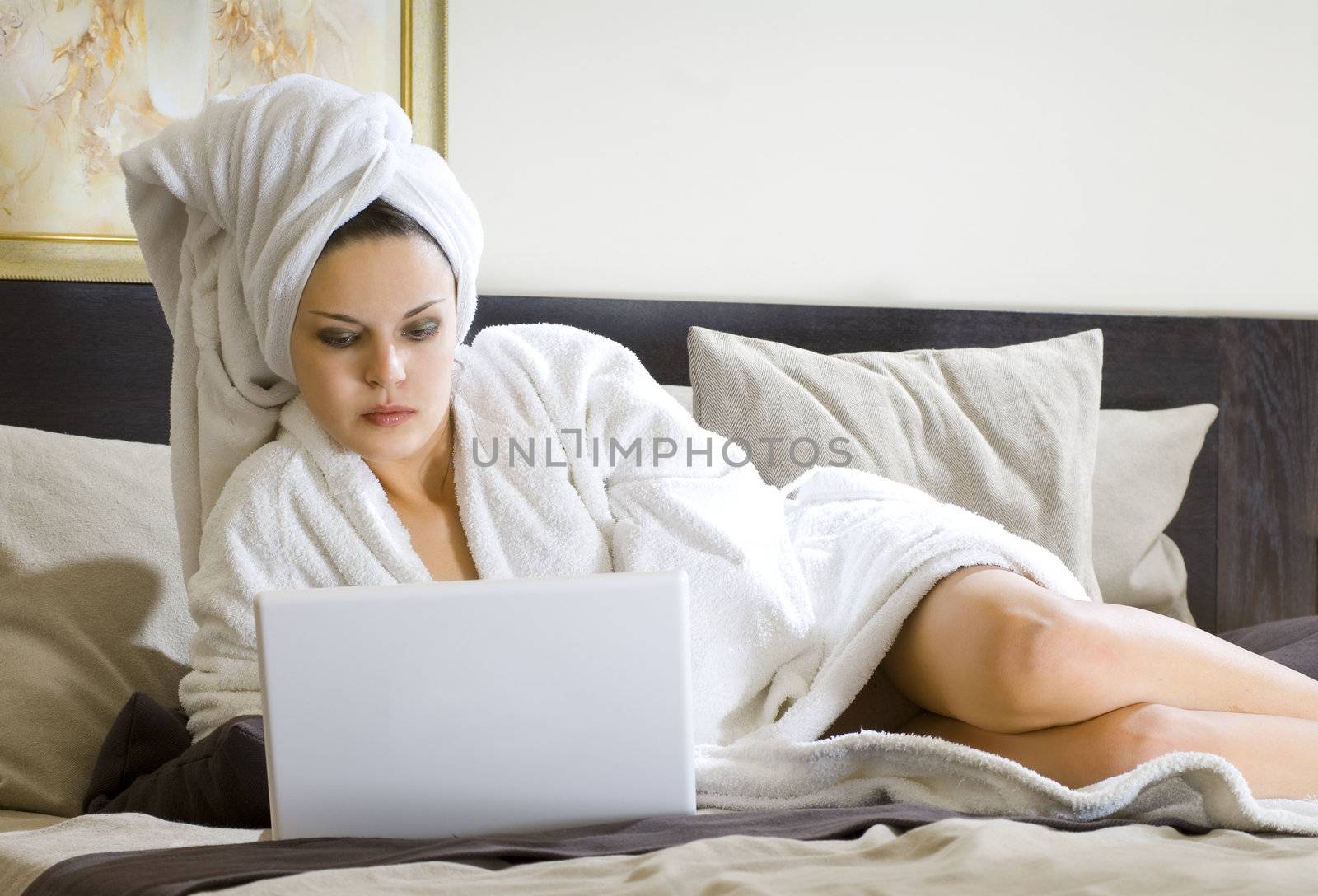 beautiful woman in white bathrobe on a bed with laptop