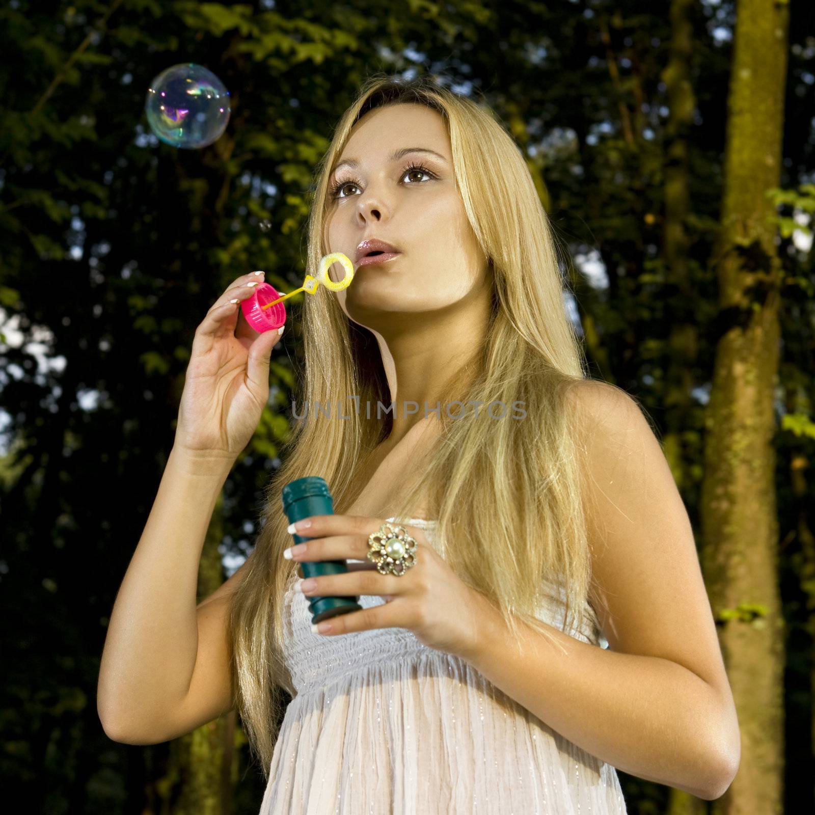 blonde young woman blowing soap bubbles in summer day