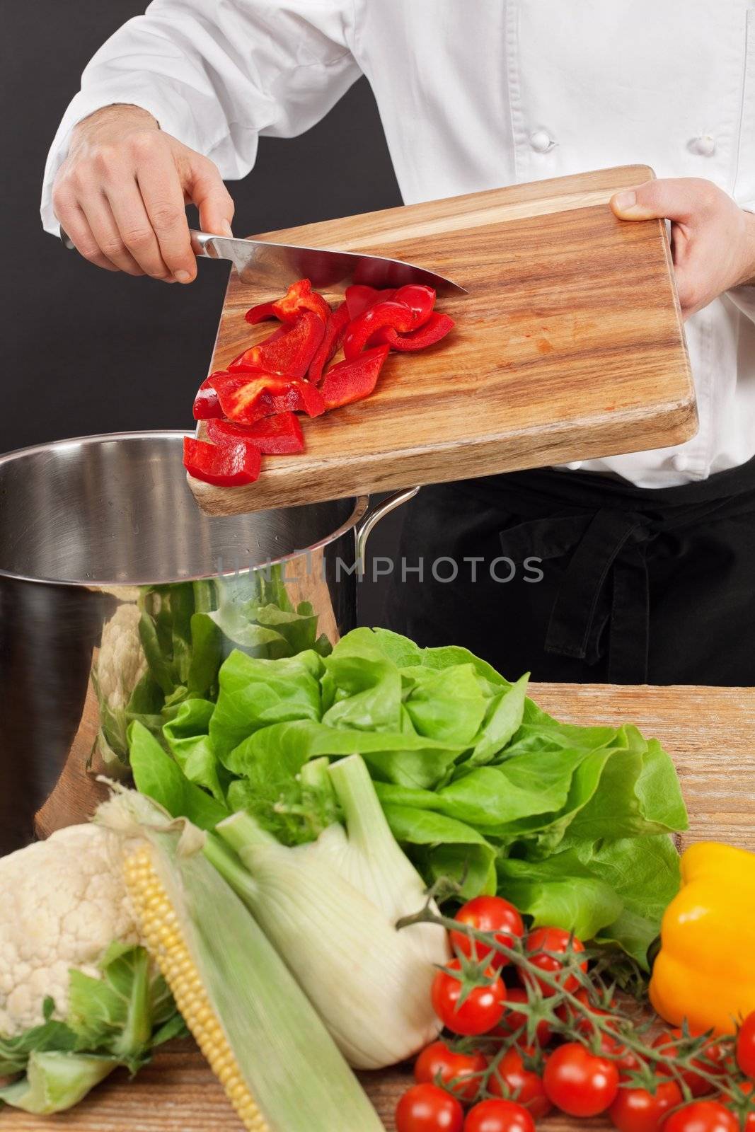 Photo of a chef putting chopped vegetables into a large saucepan.