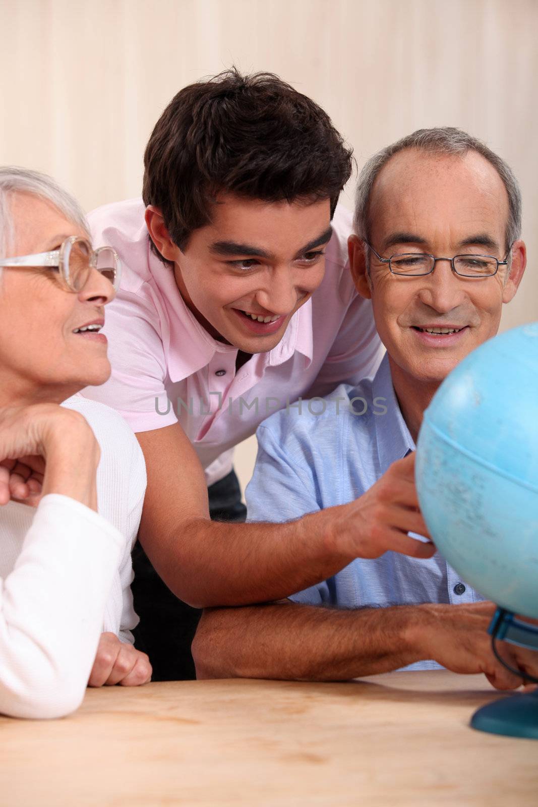 grandparents ant their grandson looking at a globe by phovoir