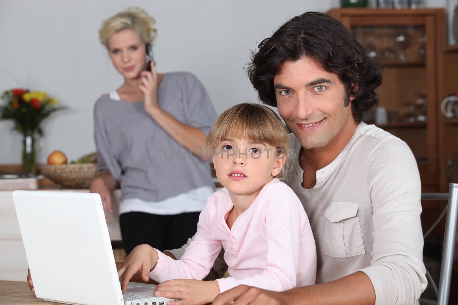 Family in kitchen with laptop by phovoir