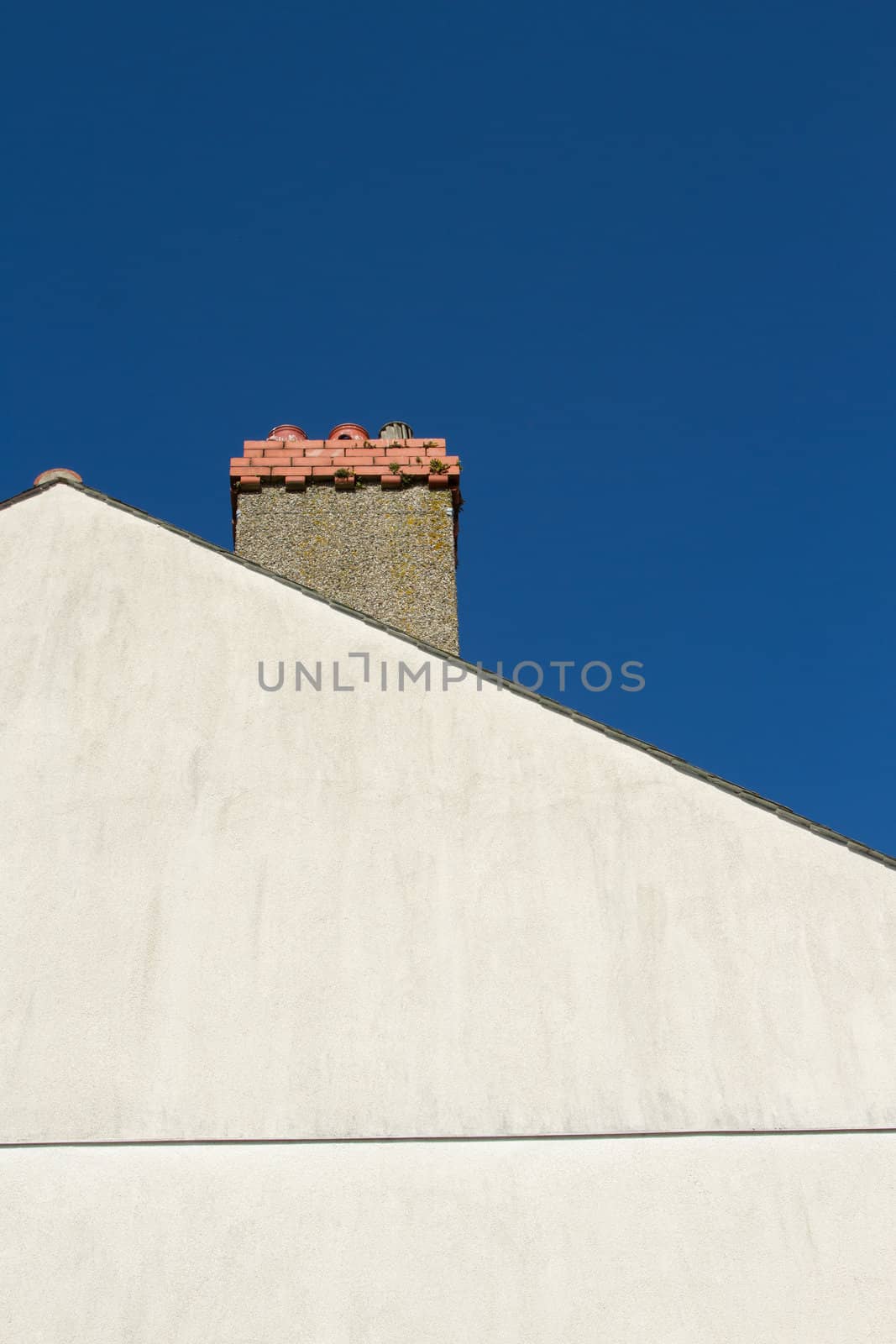 A pale coloured gable end with a chimney with ornate red brick against a blue sky.