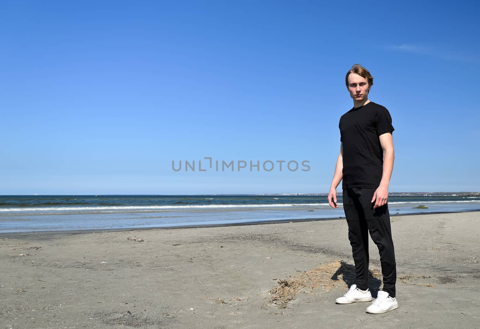 Young male in black clothes and white shoes standing on the beach