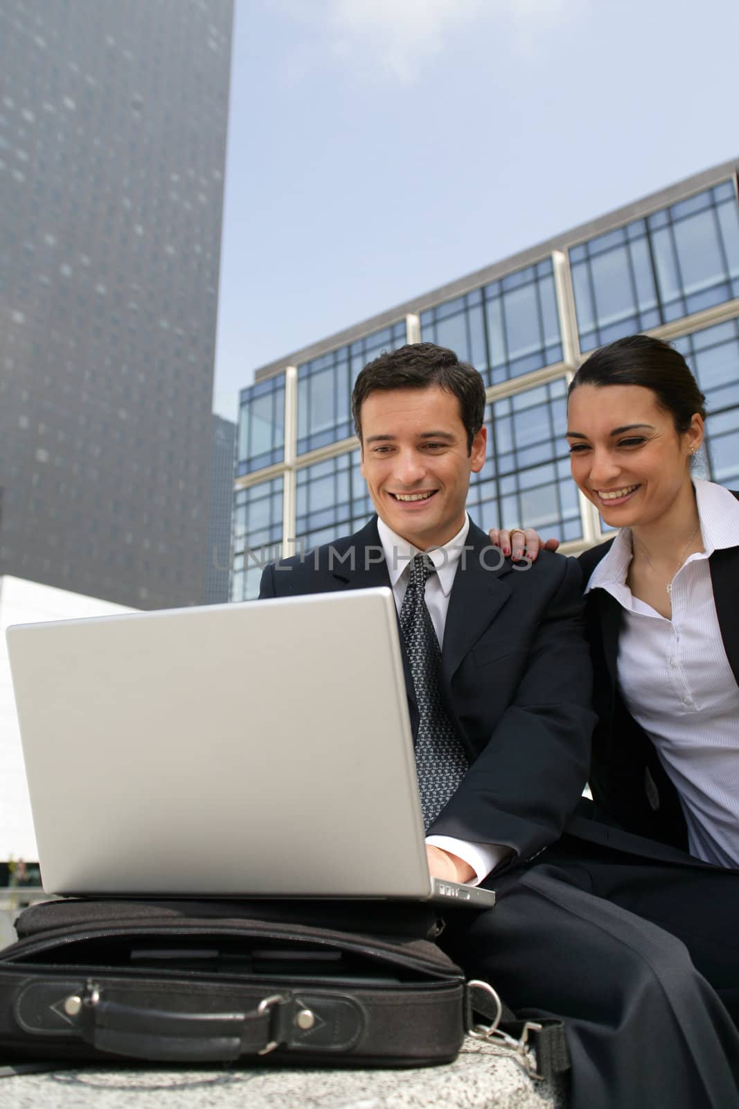 Businessman and businesswoman laughing in front of a laptop outdoors by phovoir