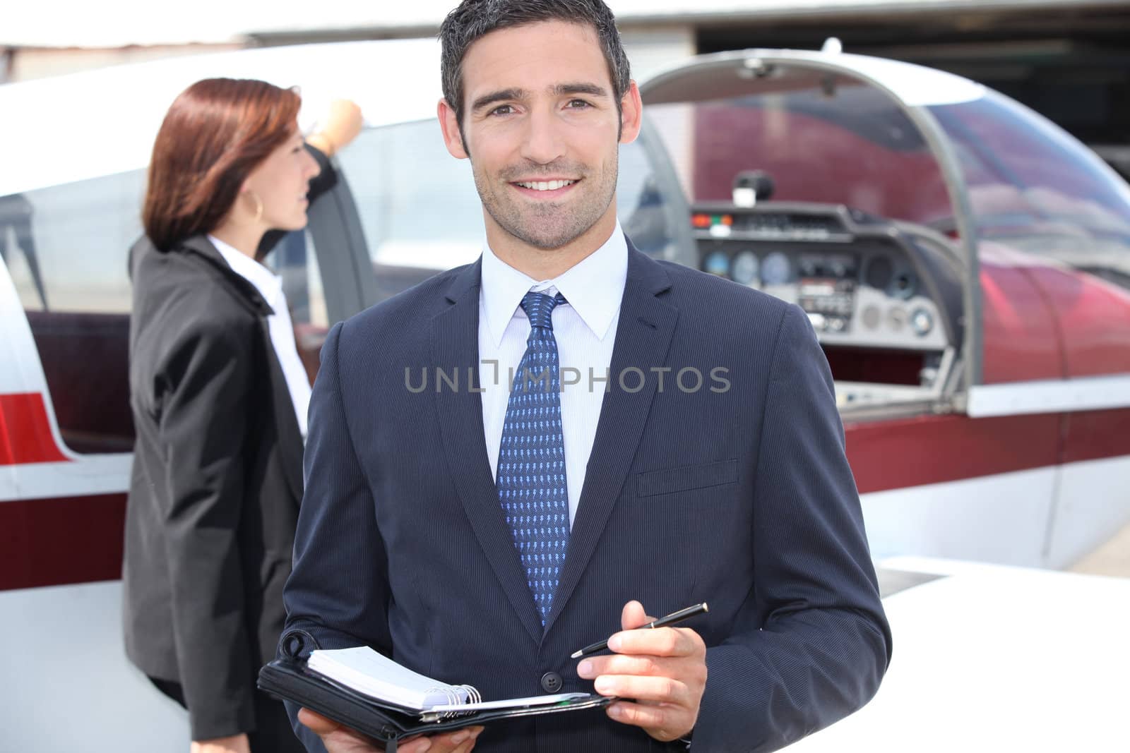 Man in suit taking notes in front of an airplane by phovoir