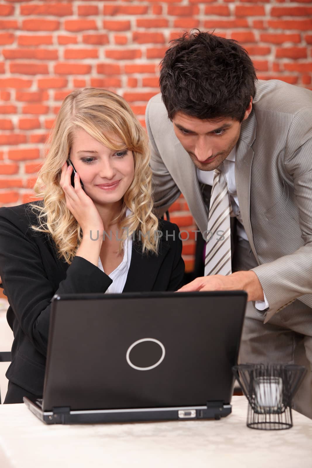 Business couple in a restaurant using a laptop and phone by phovoir