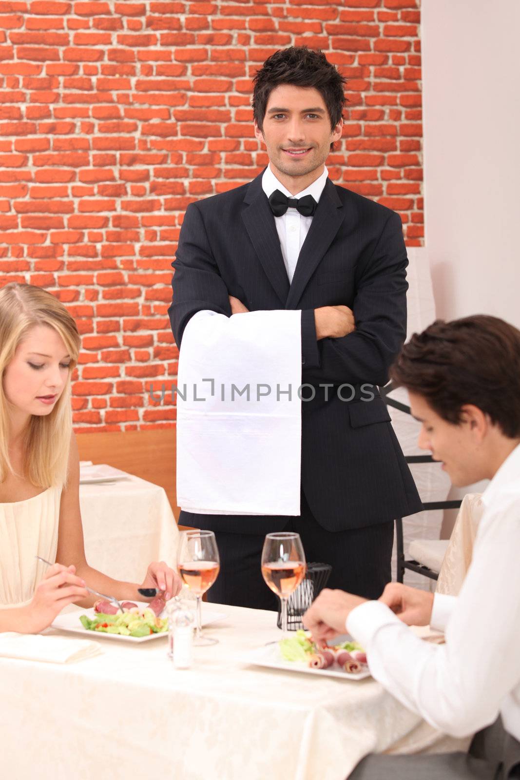 Waiter stood by couple enjoying meal by phovoir
