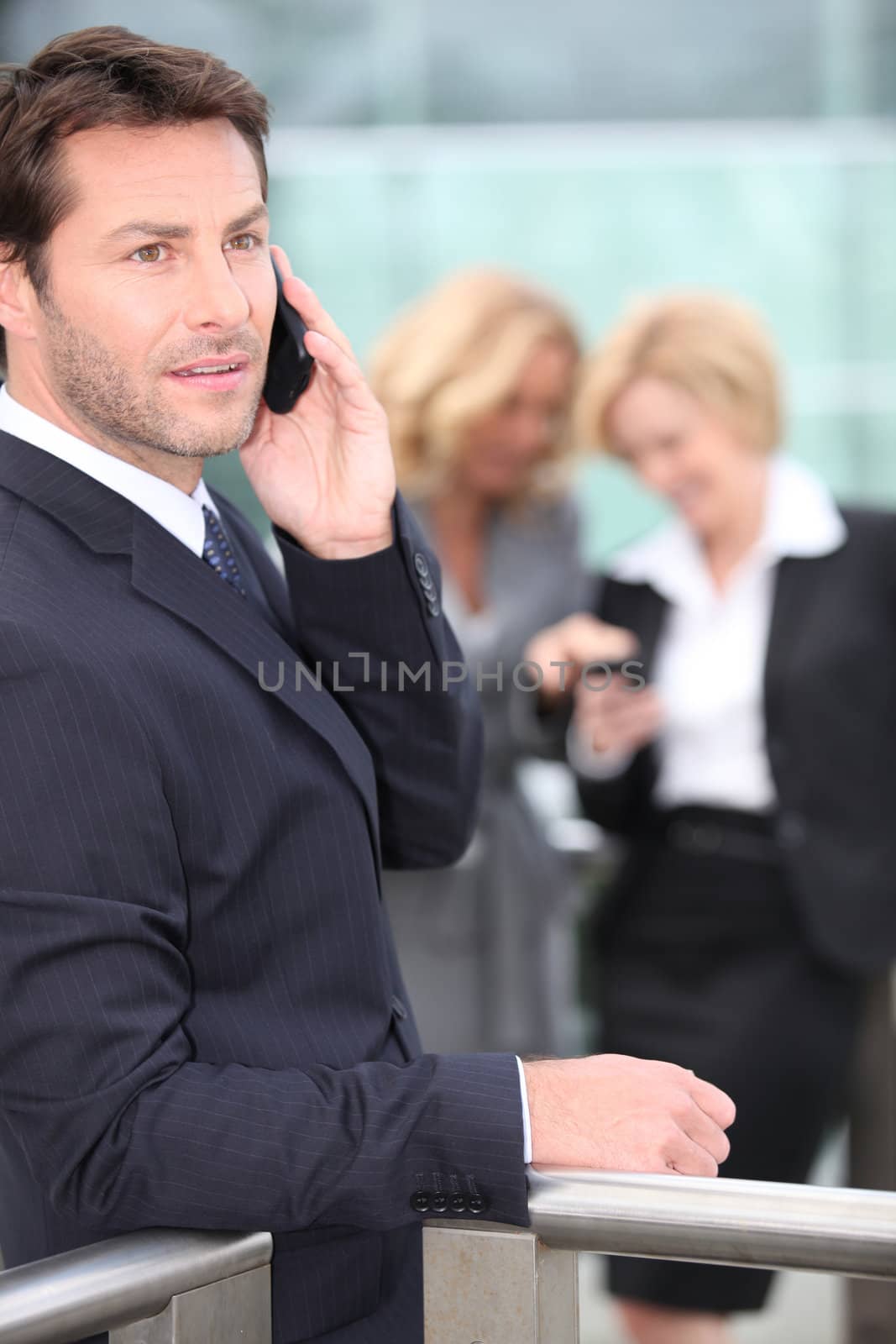 Businessman holding mobile telephone with colleagues in background by phovoir