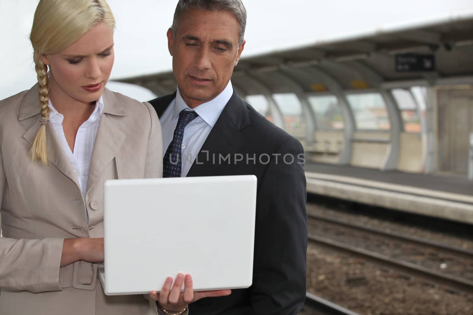 Business couple with a laptop on a railway platform by phovoir