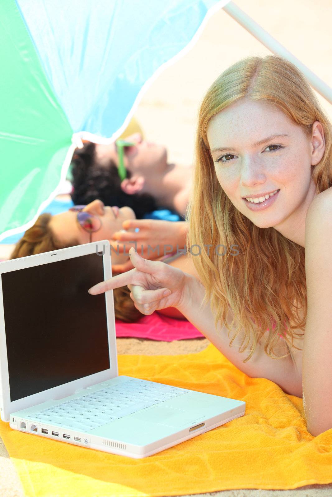 pretty girl pointing her laptop while her friends are tanning