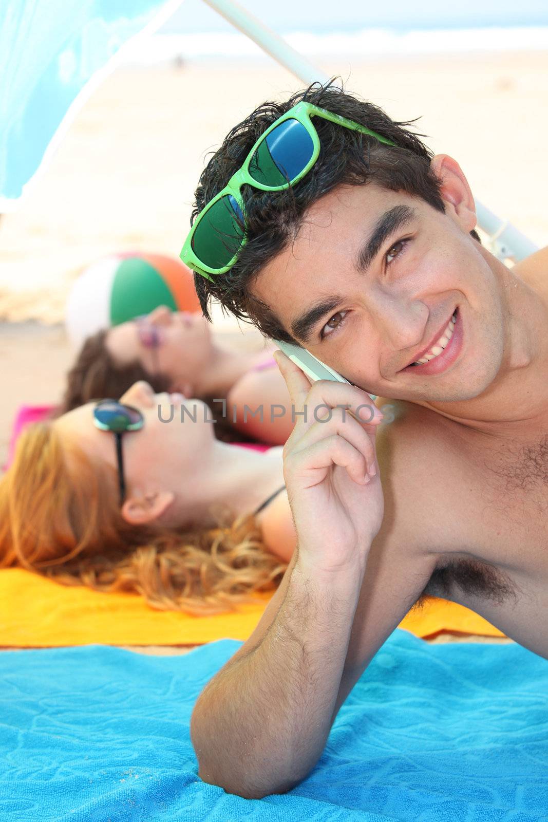 Young man using a cellphone on the beach by phovoir