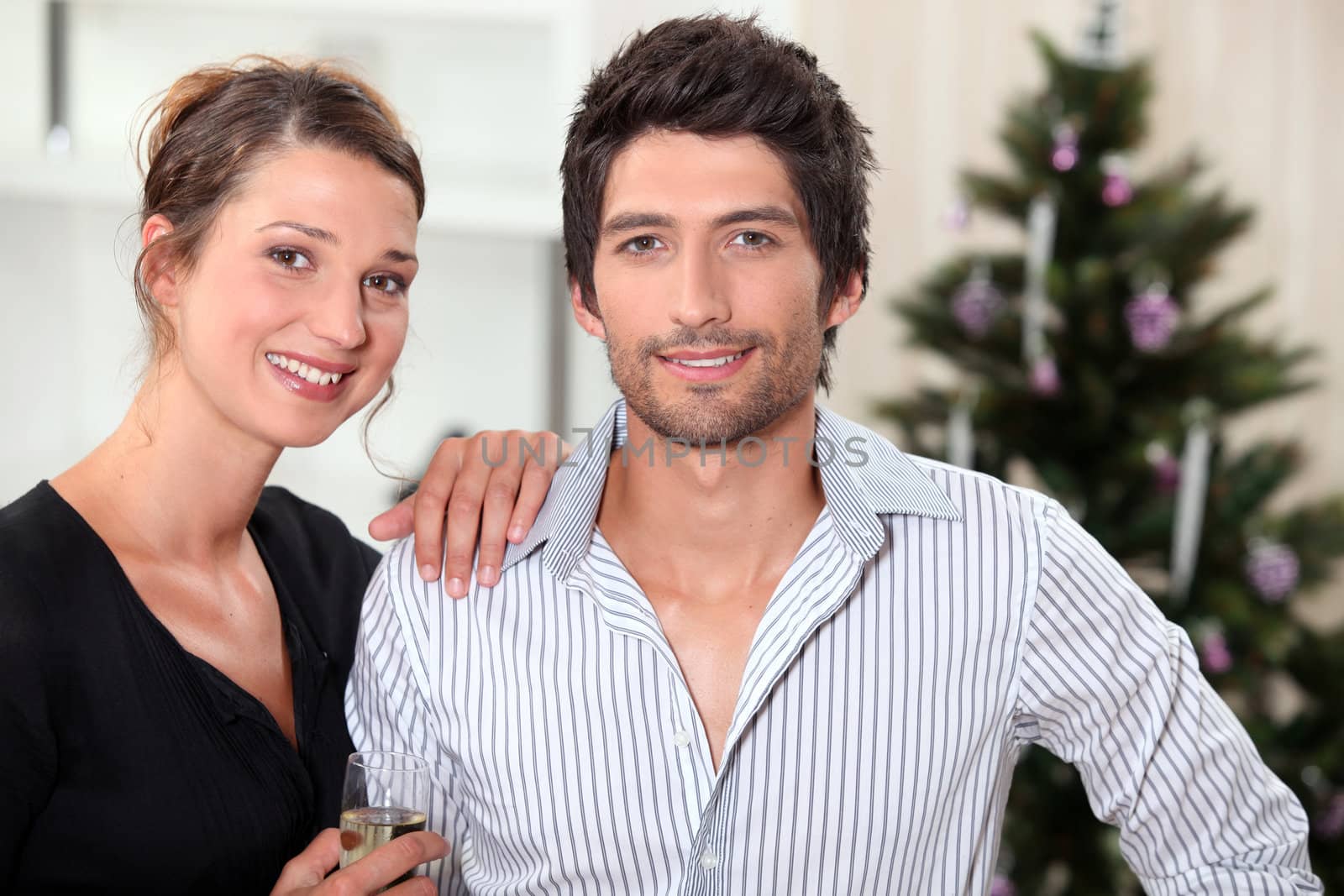 a couple behind a Christmas tree inside an apartment