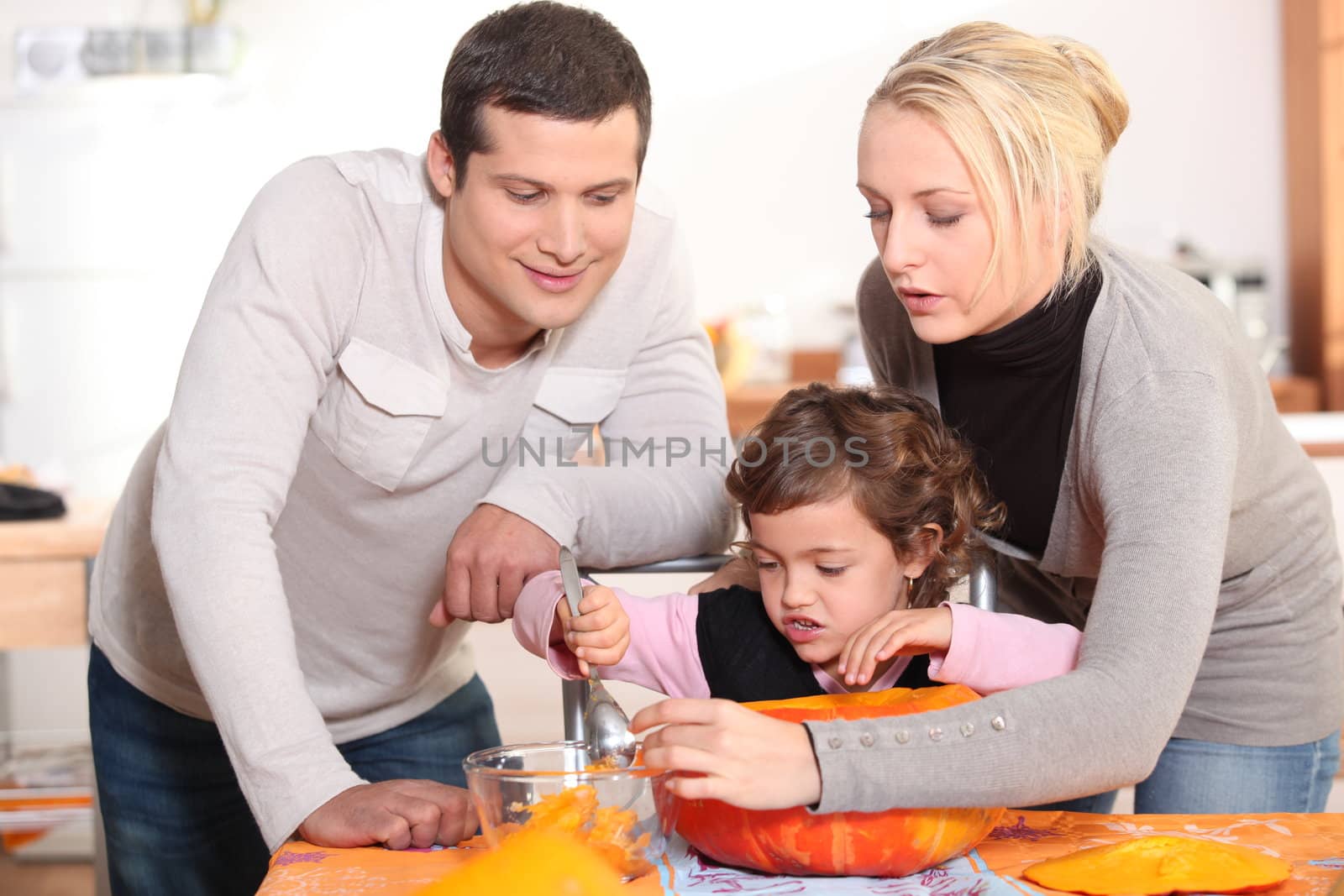 Parents carving a pumpkin with their daughter by phovoir