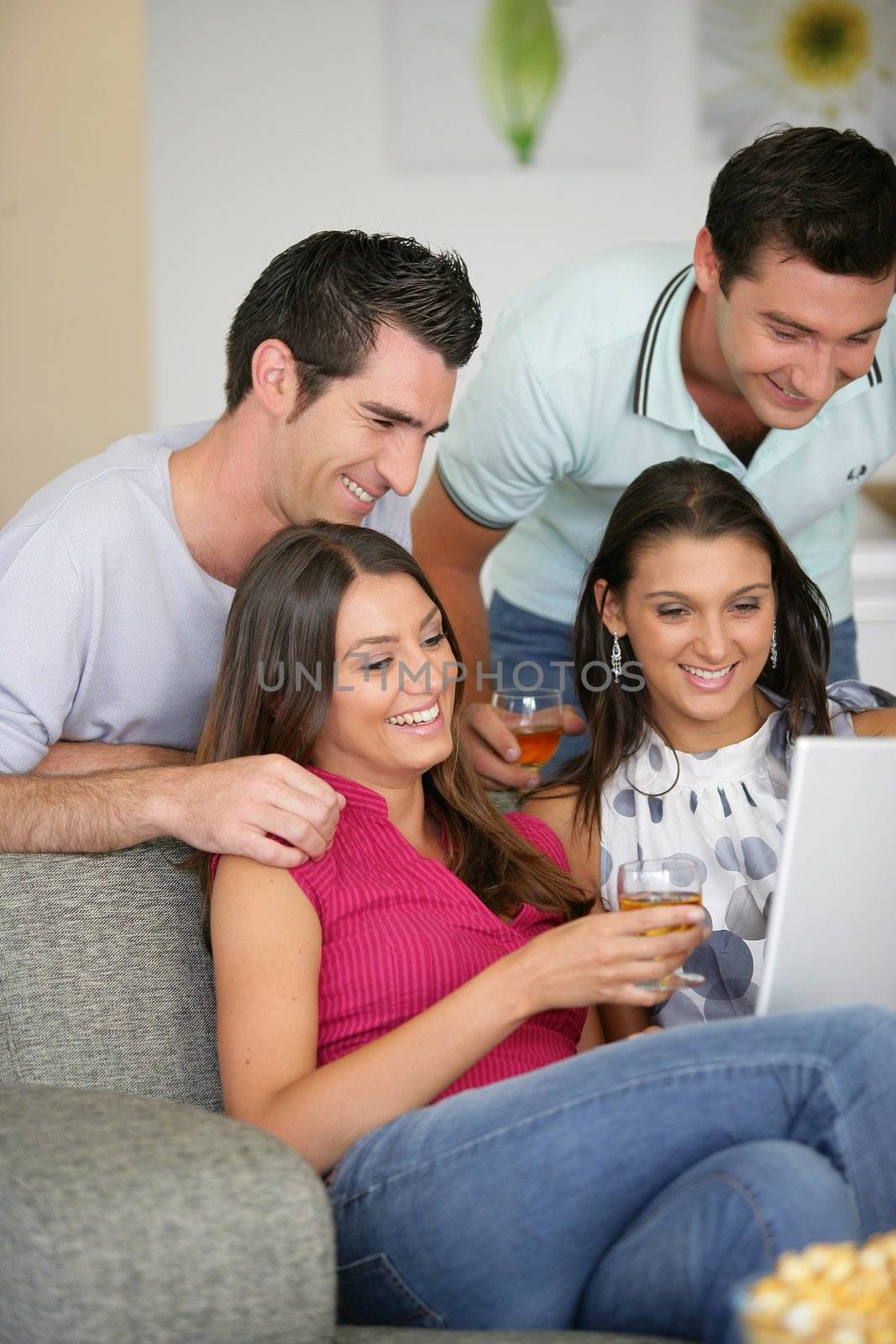 Two couples at home laughing at a laptop by phovoir