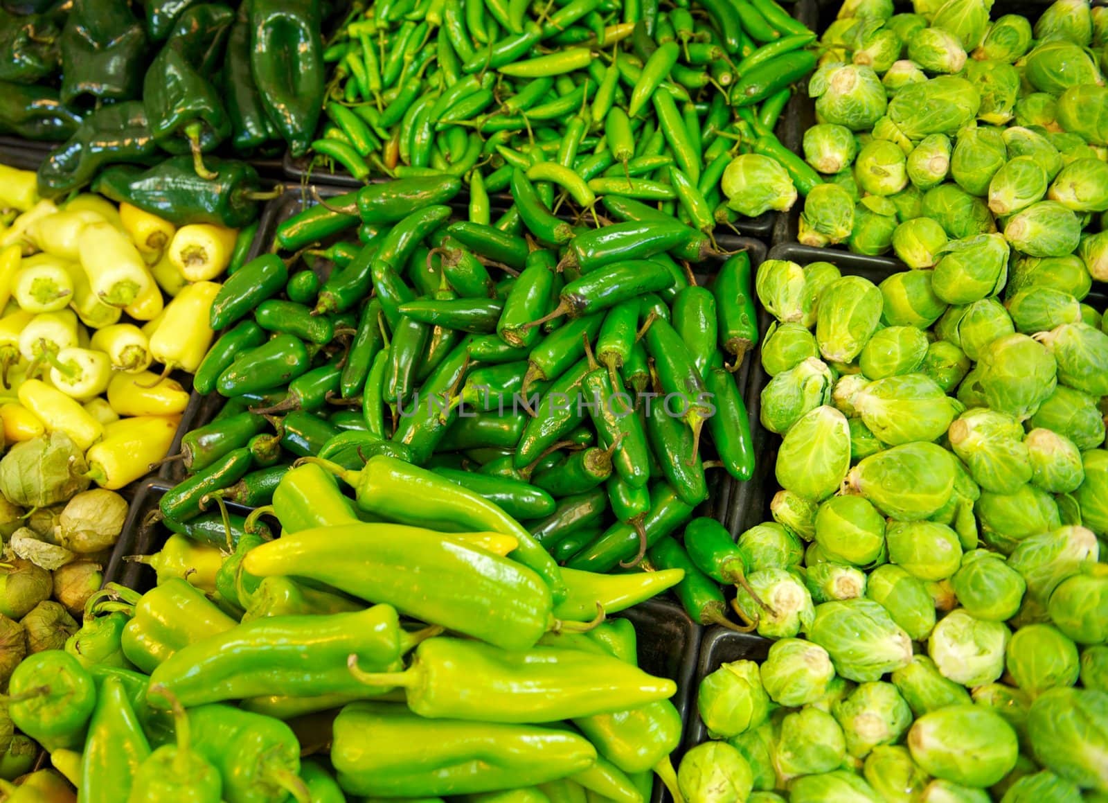 A grocery store's produce section with bins overflowing with chilies, peppers and brussel sprouts