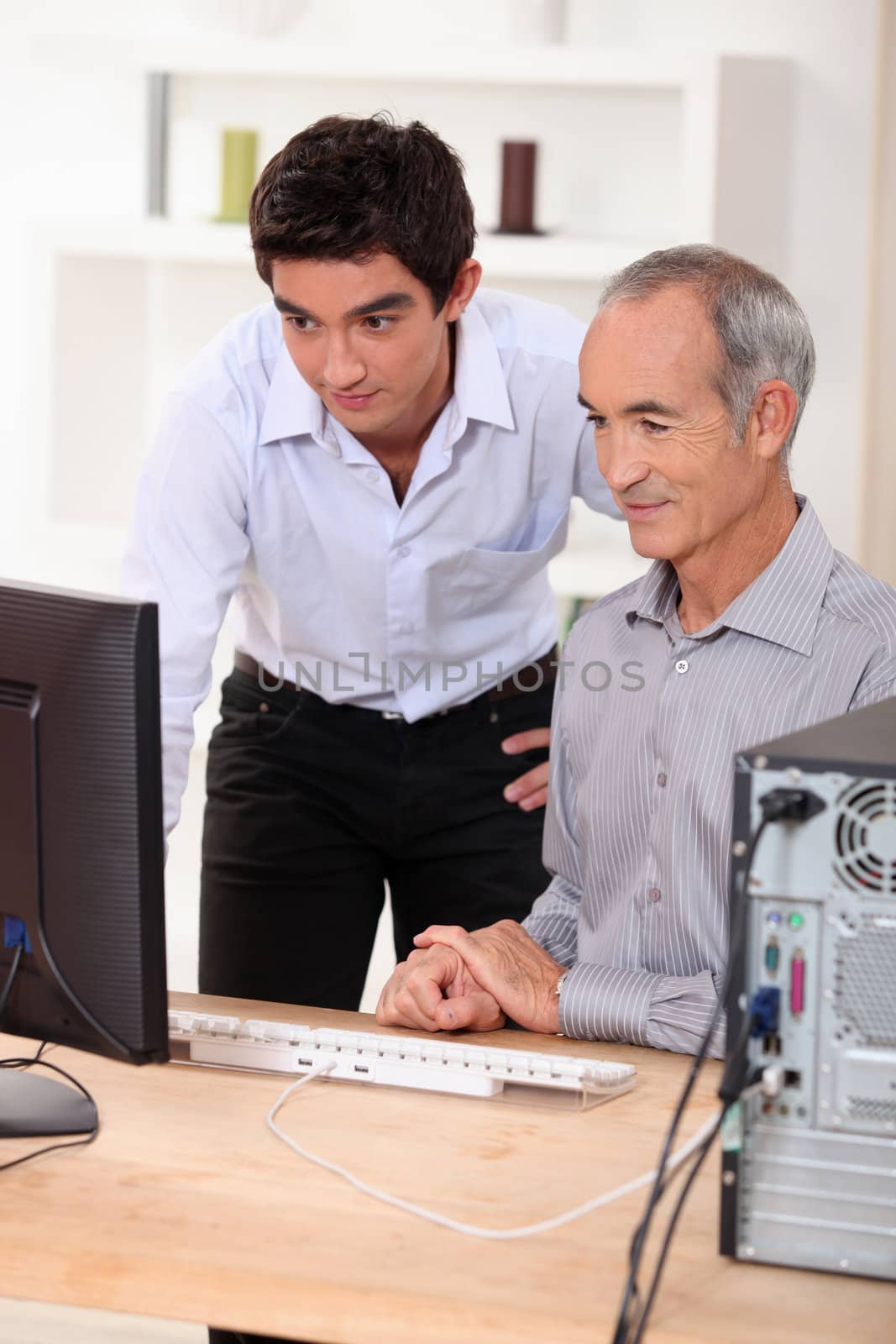 grandson showing his grandfather how to use a computer by phovoir