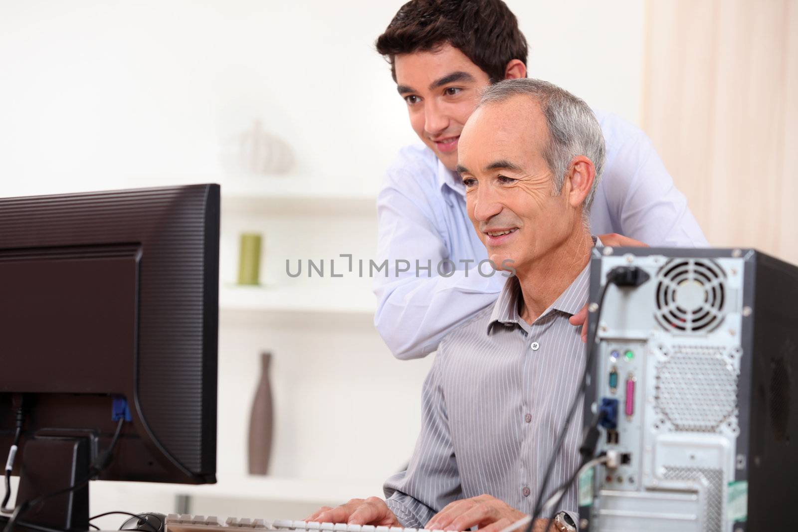 Young man teaching an elderly man computer skills