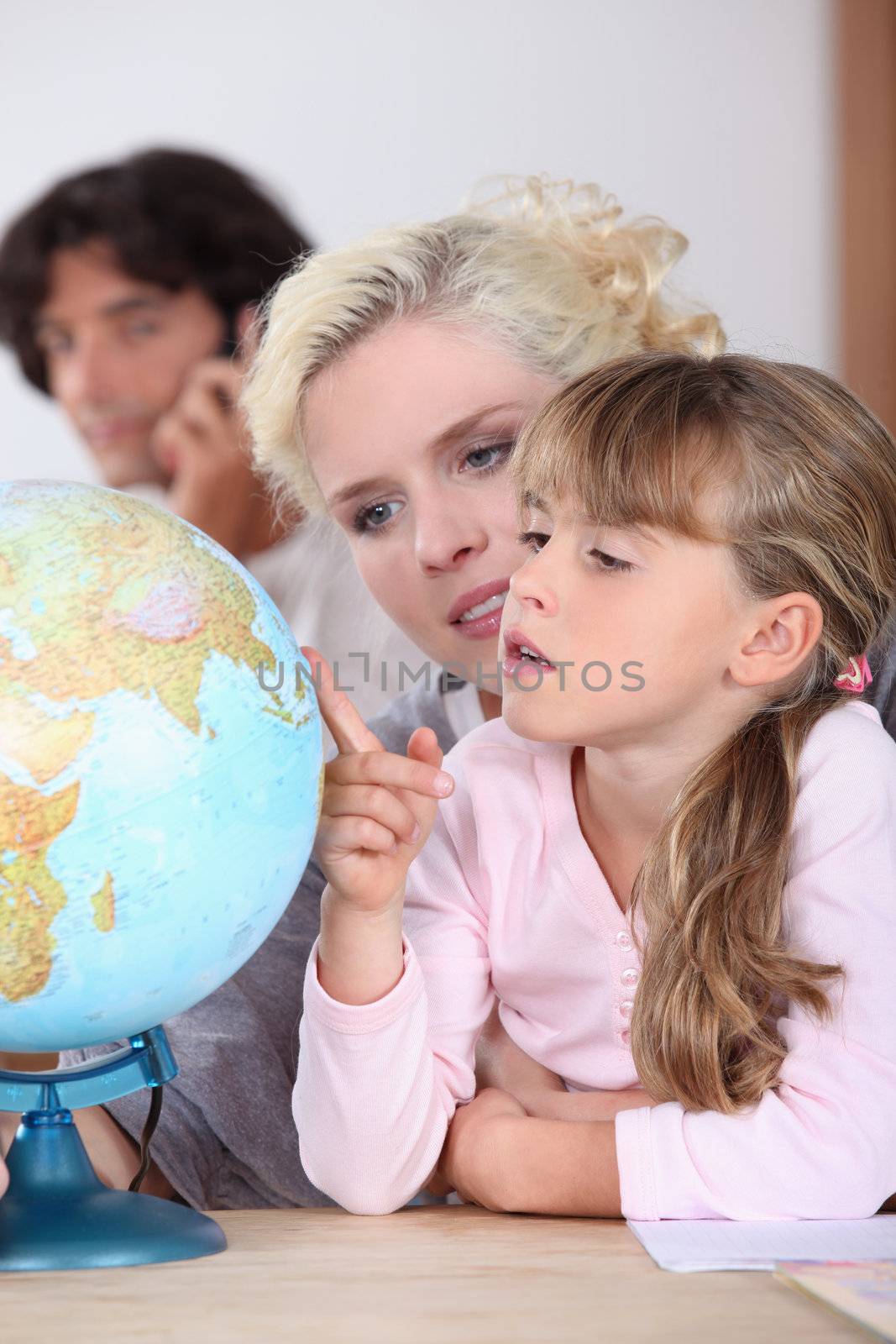 a mother is showing to her daughter some country on a globe, her husband is on the phone by phovoir
