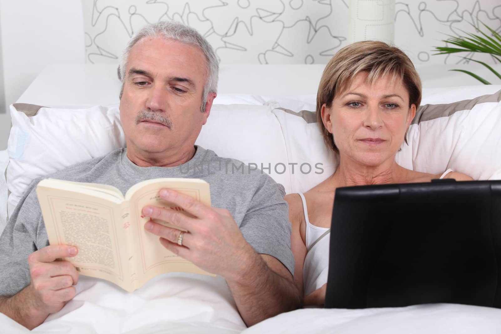 Man reading in bed while his wife surfs the internet