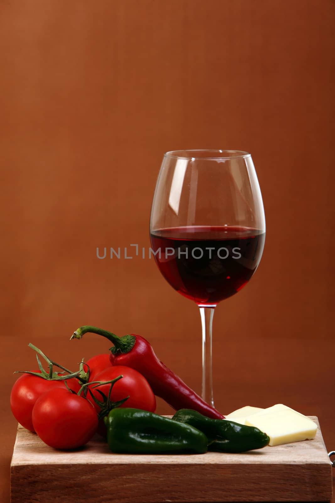 Red wine on brown background with cheese and vegetables