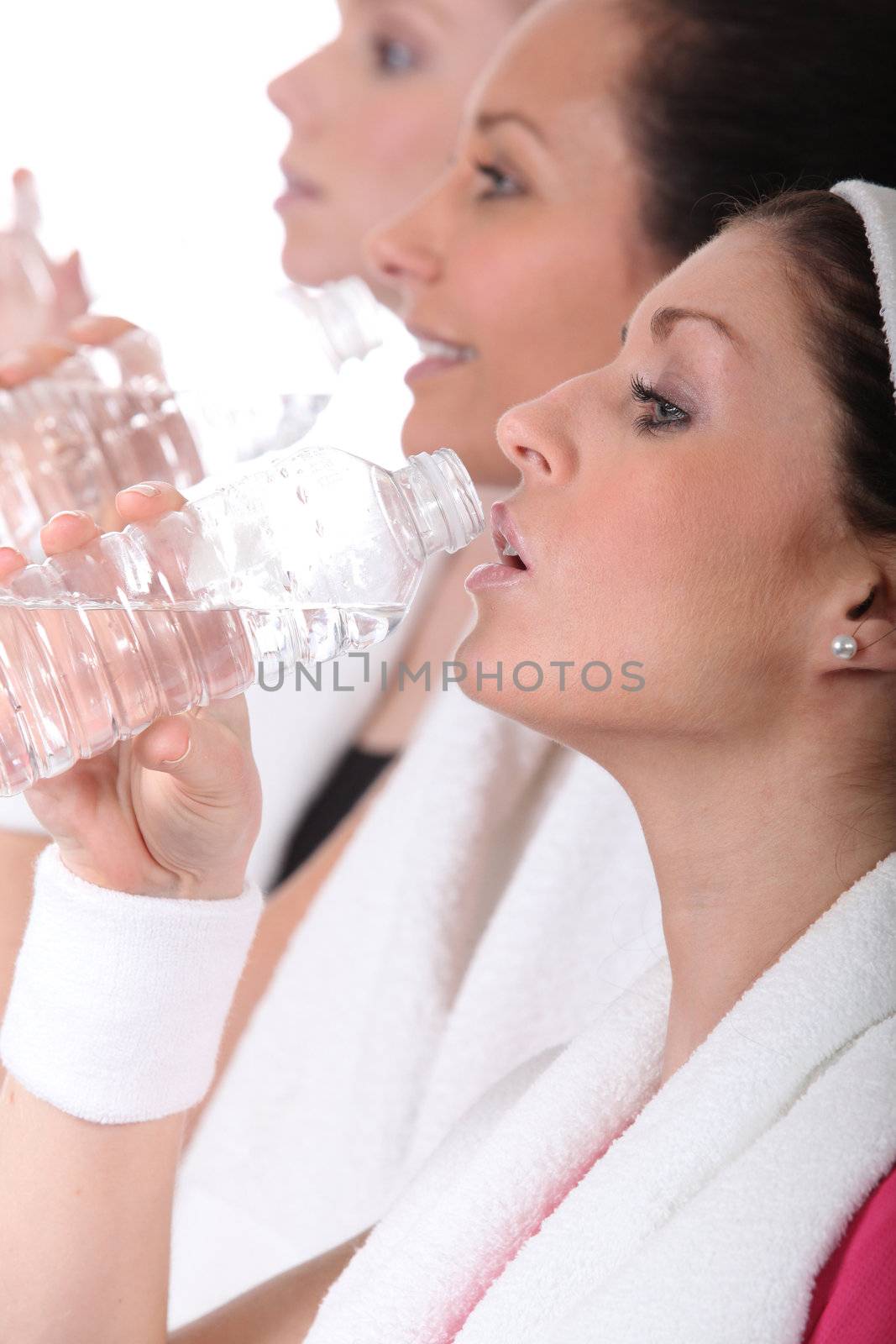 Women in gym drinking from water bottles by phovoir