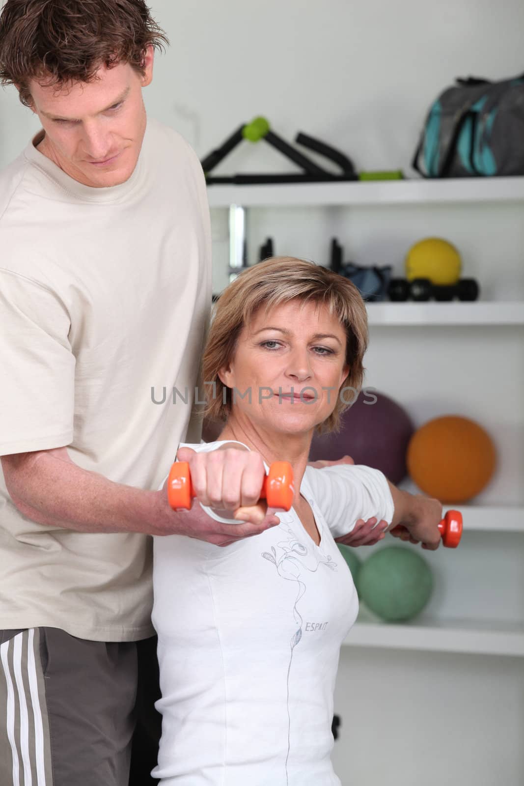 Woman using dumbbells with a personal trainer by phovoir