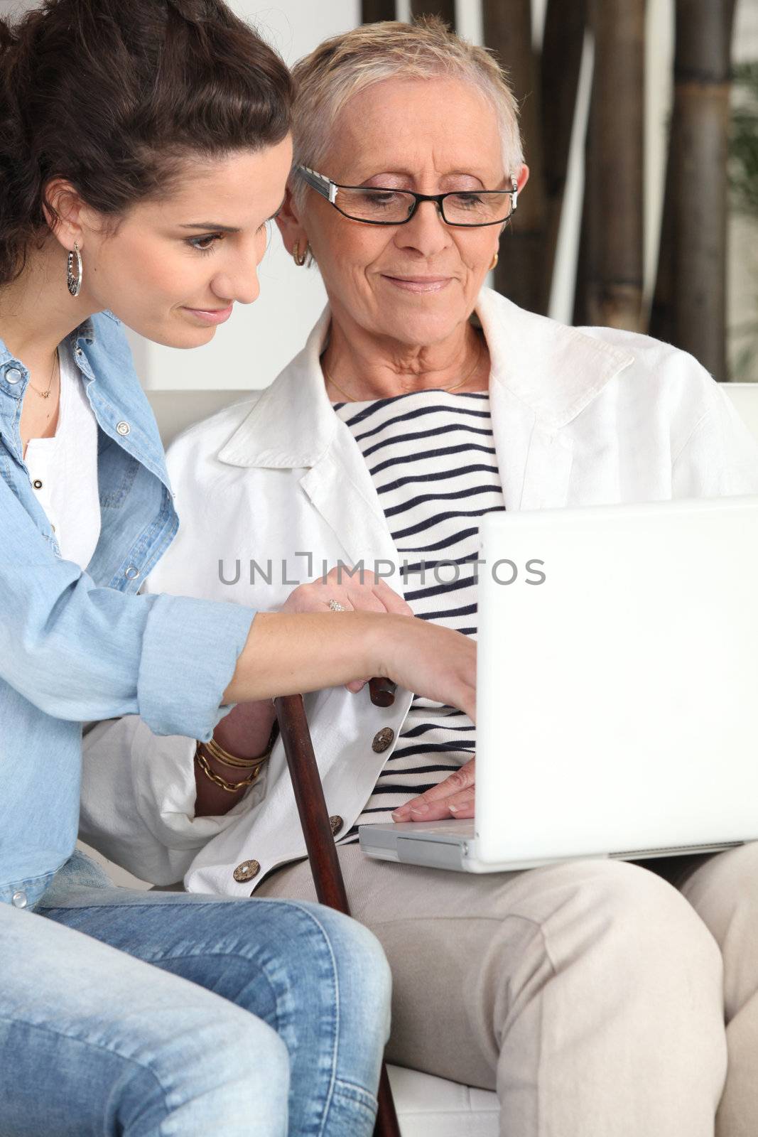 Young woman helping an elderly lady navigate the internet by phovoir