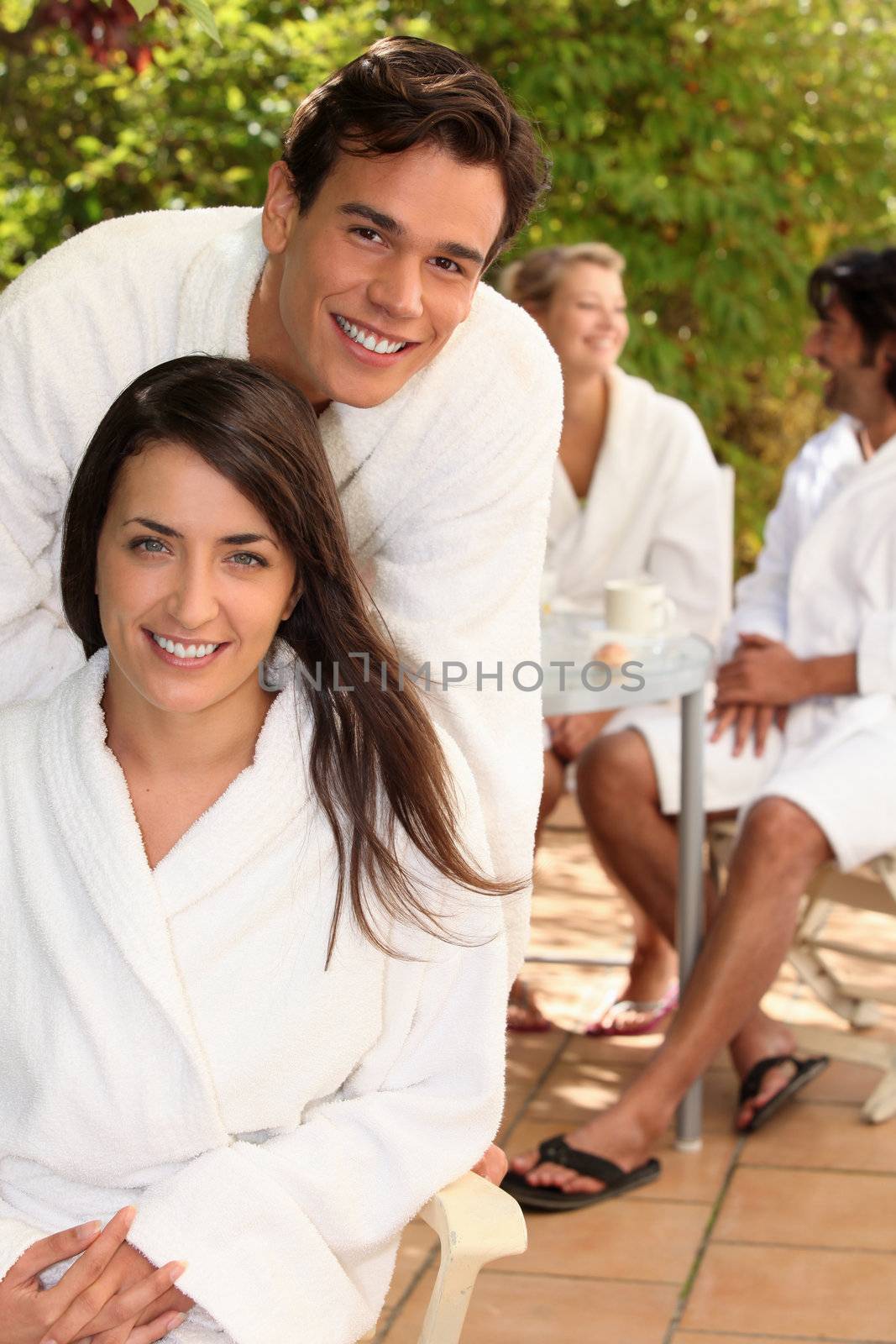 Couple with friends sitting on a terrace in toweling robes by phovoir