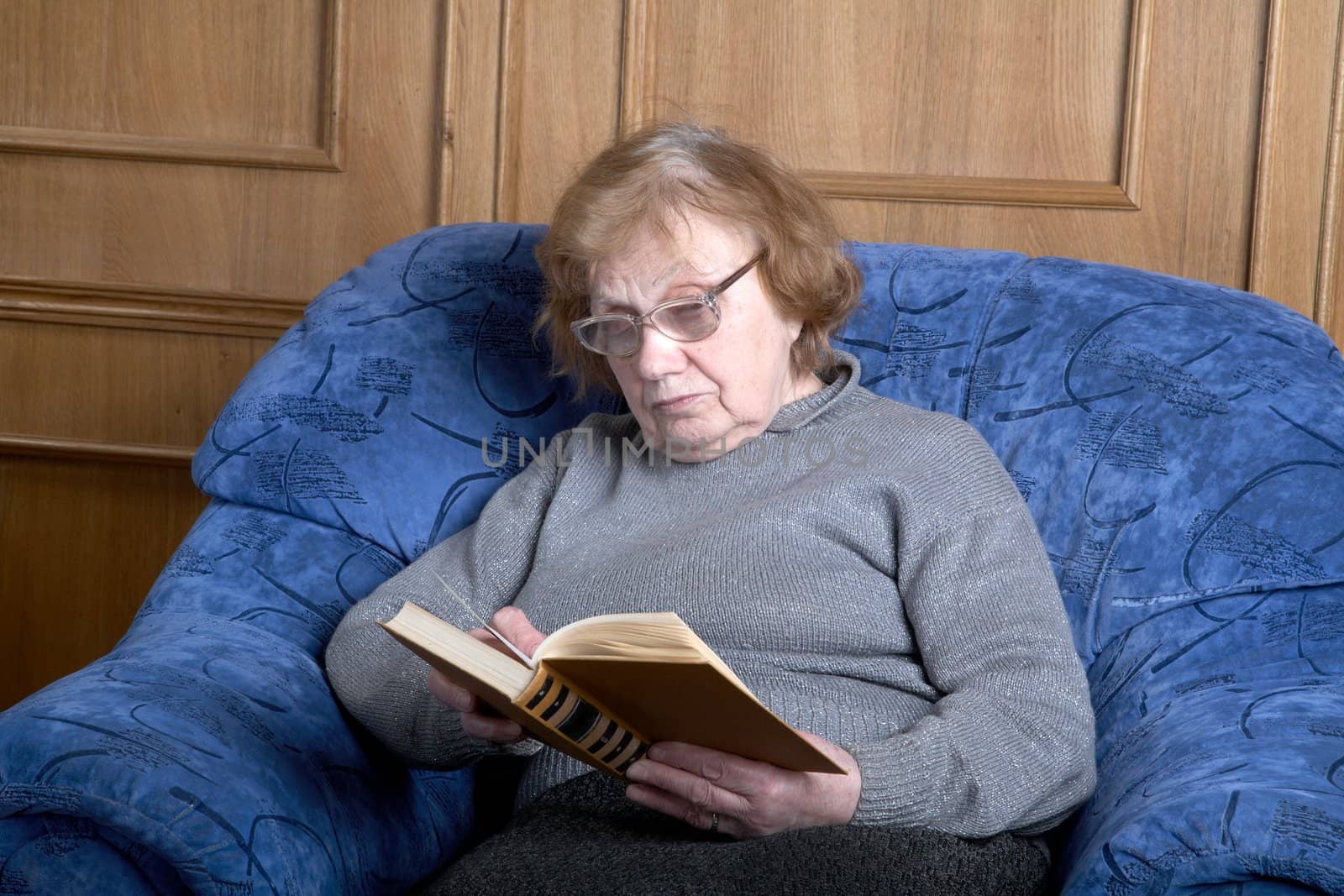 The old woman sits in an armchair and reads the book