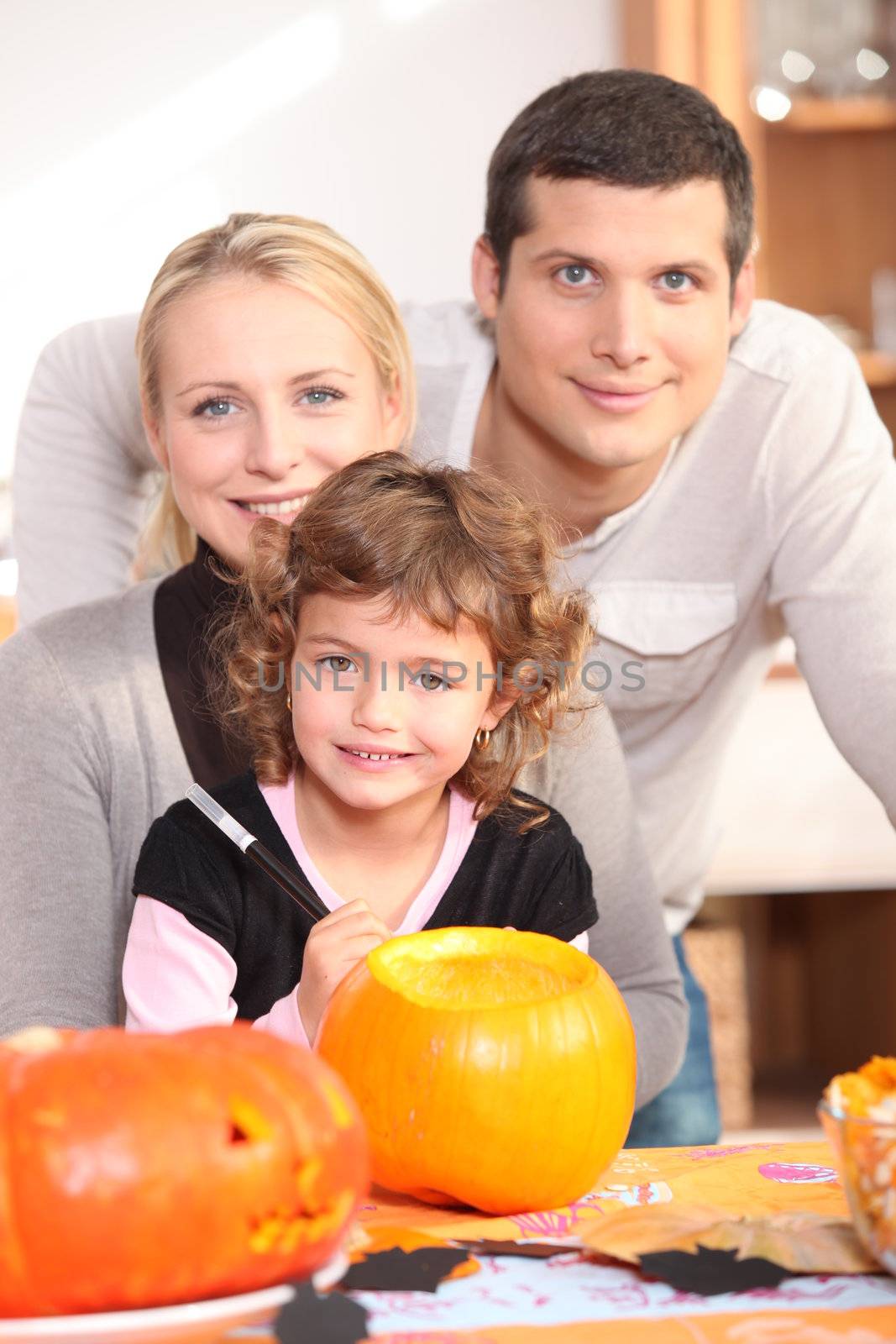 Little girl with parents preparing pumpkin for Halloween by phovoir
