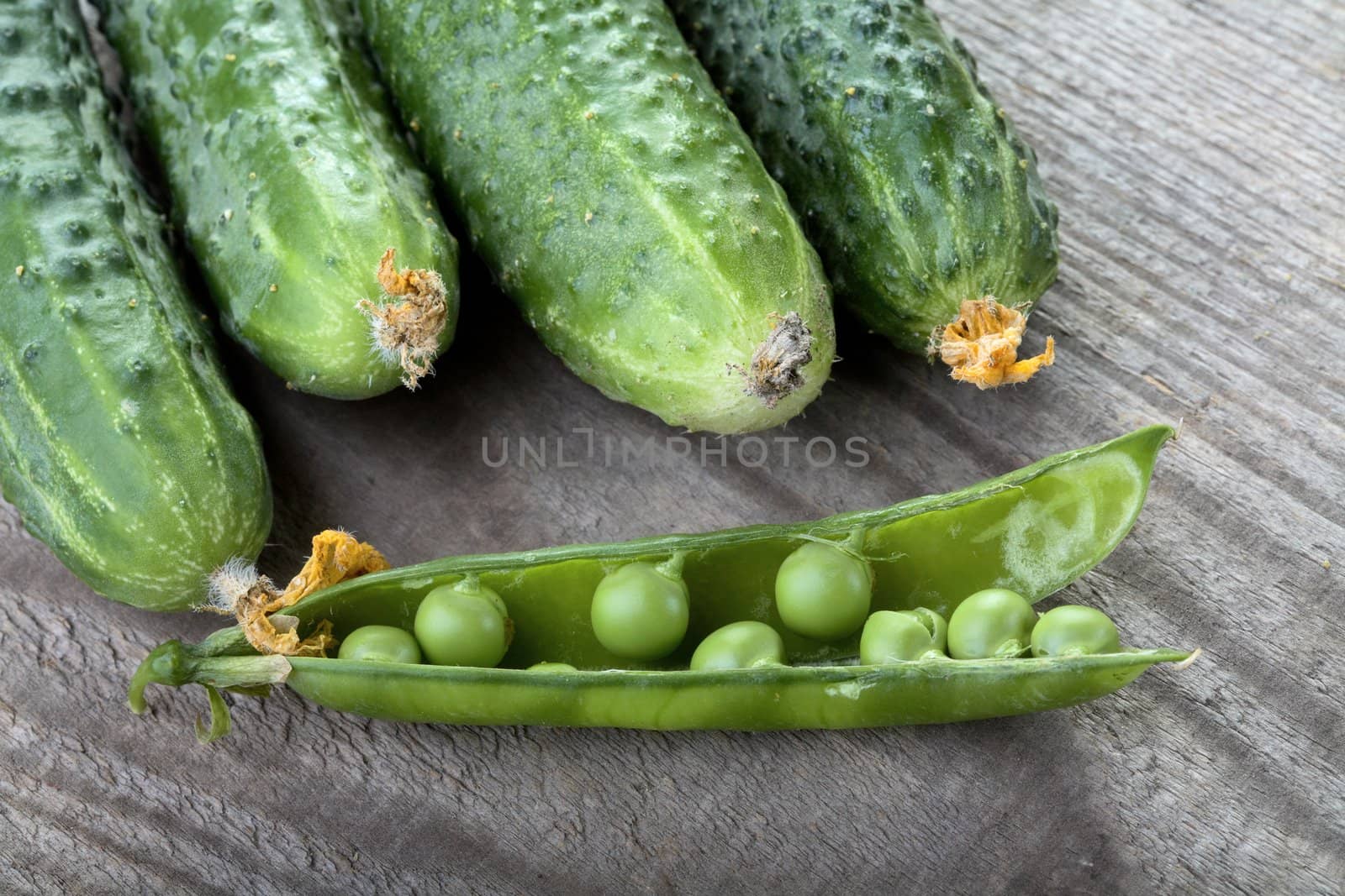 Green cucumbers and peas pod on a table from unplaned boards