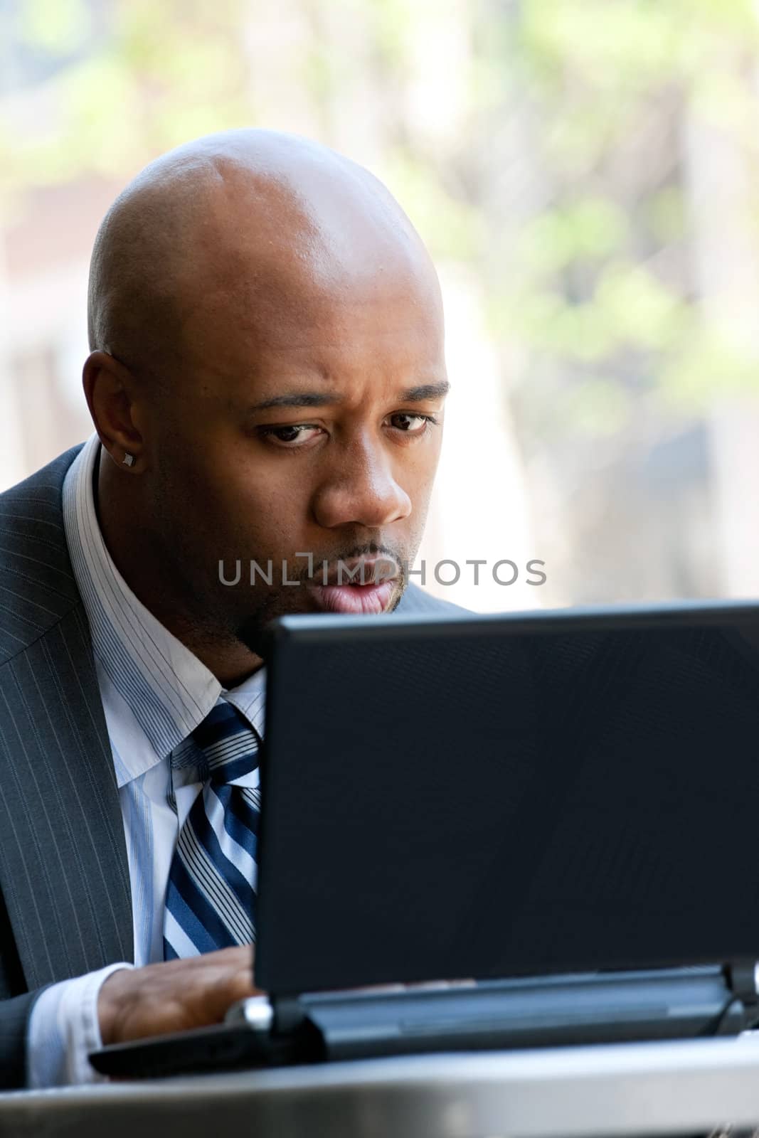 A business man in his early 30s working on his laptop or netbook computer outdoors with a surprised or shocked expression on his face.