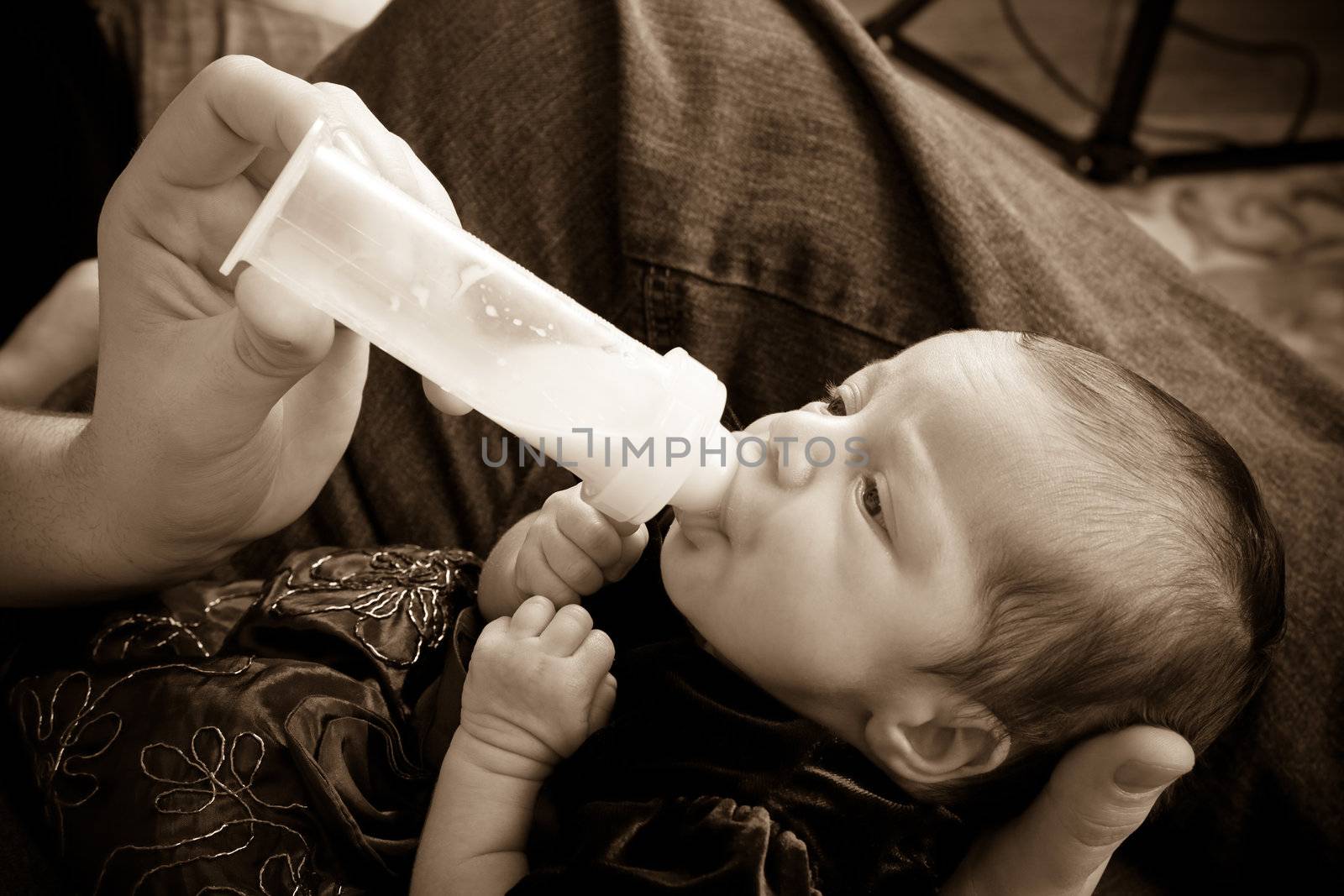 Newborn infant feeds on a bottle of baby formula while being held by her mother.