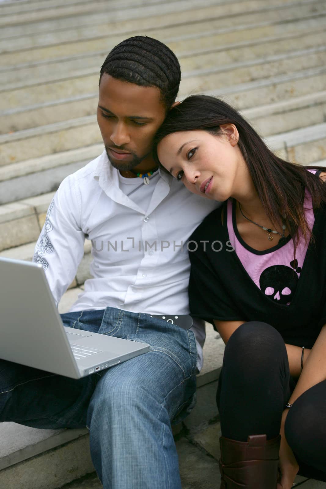 Young couple on some steps with a laptop by phovoir