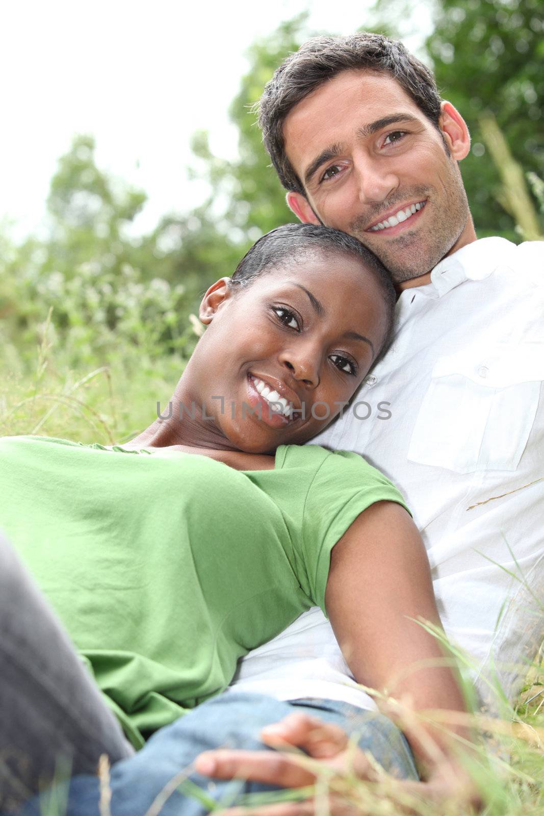 An interracial couple lying on grass.