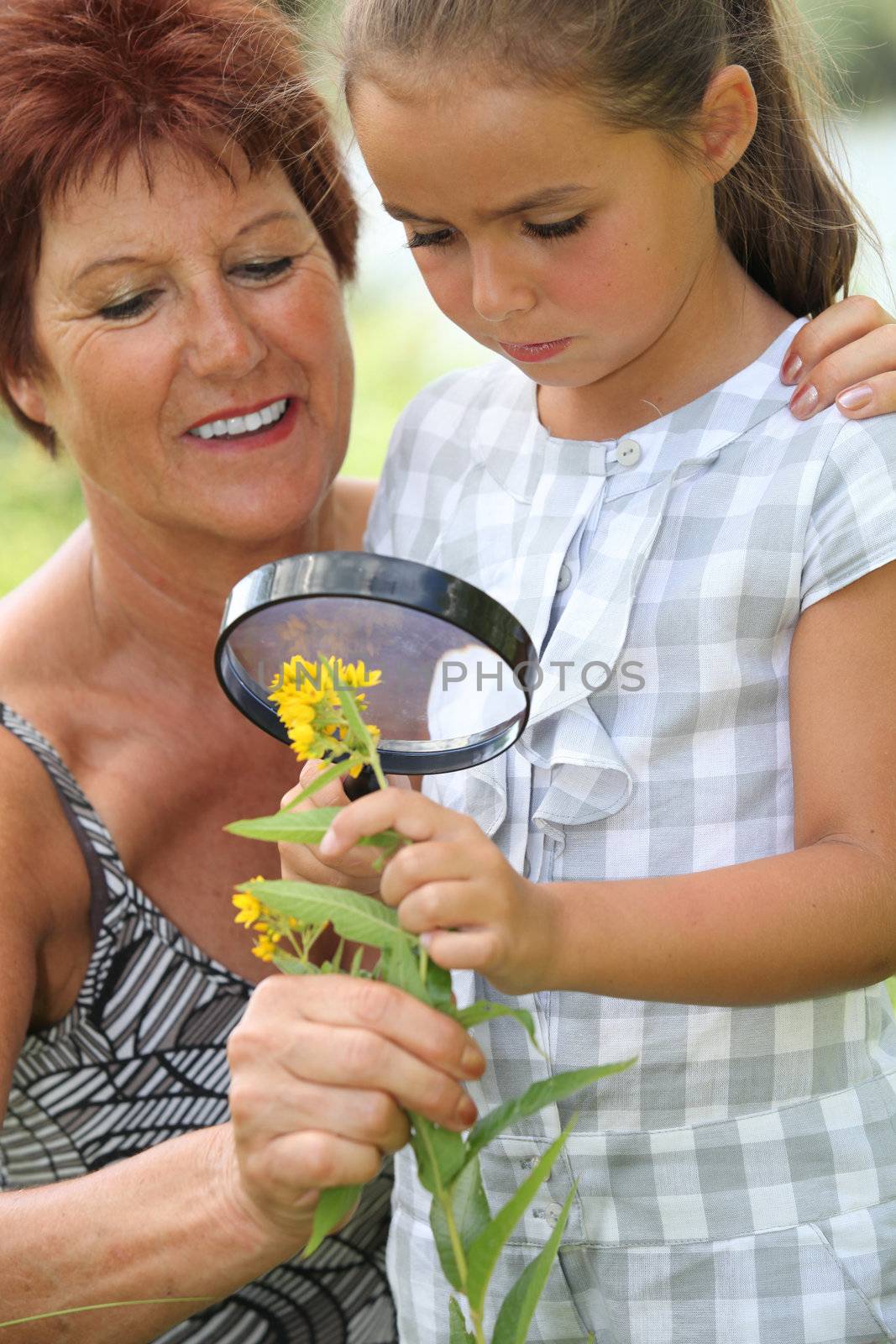 a 55 years old woman and a little looking a yellow flower with a magnifying glass