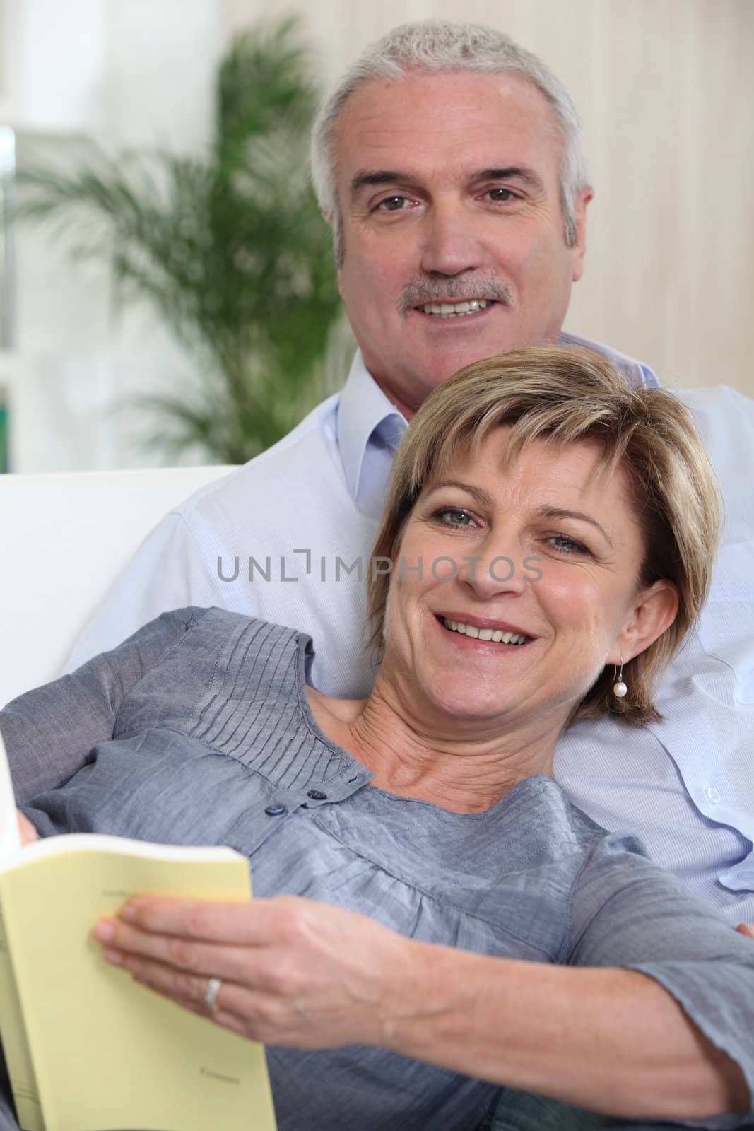 Mature couple on a sofa reading a book by phovoir