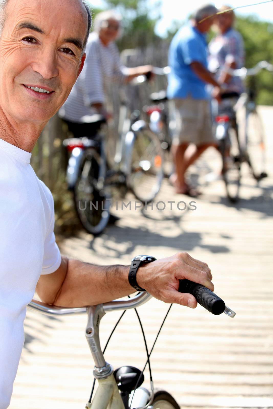 Senior man with a bicycle and his friends in the background by phovoir