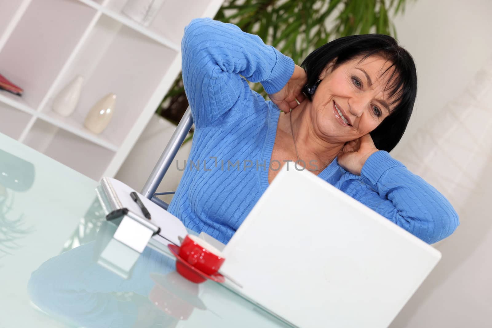A middle age woman stretching in front of her computer.