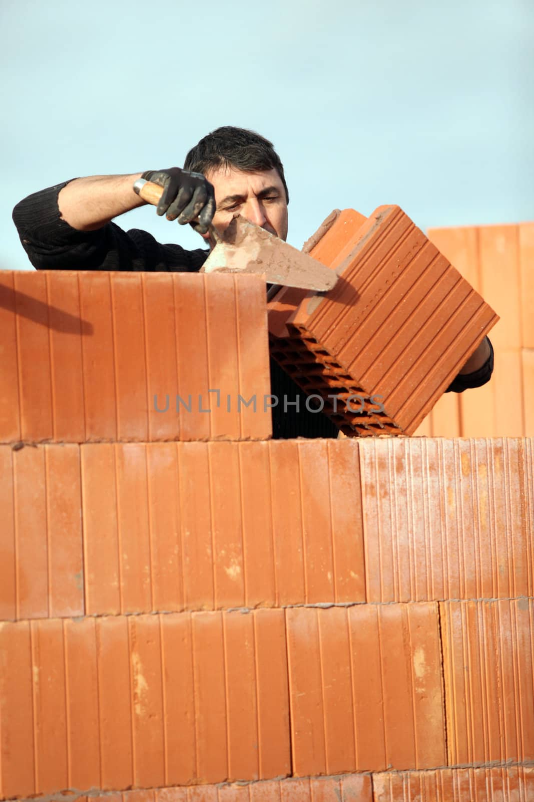 bricklayer in construction site erecting red brick wall