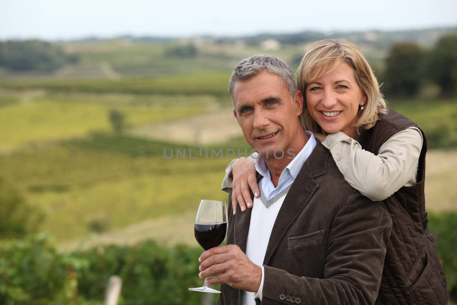 Couple with wine glass in front of vineyard by phovoir