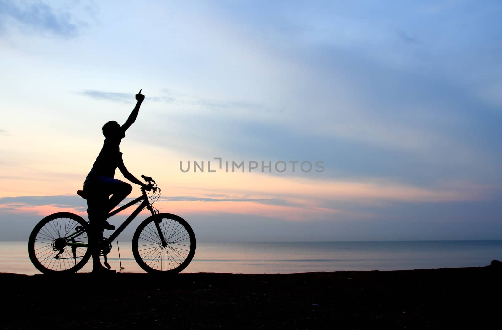 Silhouette of man riding bicycle with beautiful lake near by at sunset