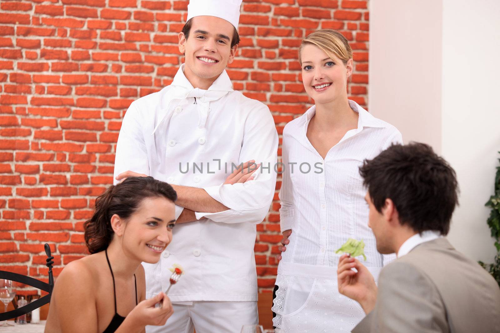 a couple dining at restaurant, a cook and a waitress behind them by phovoir