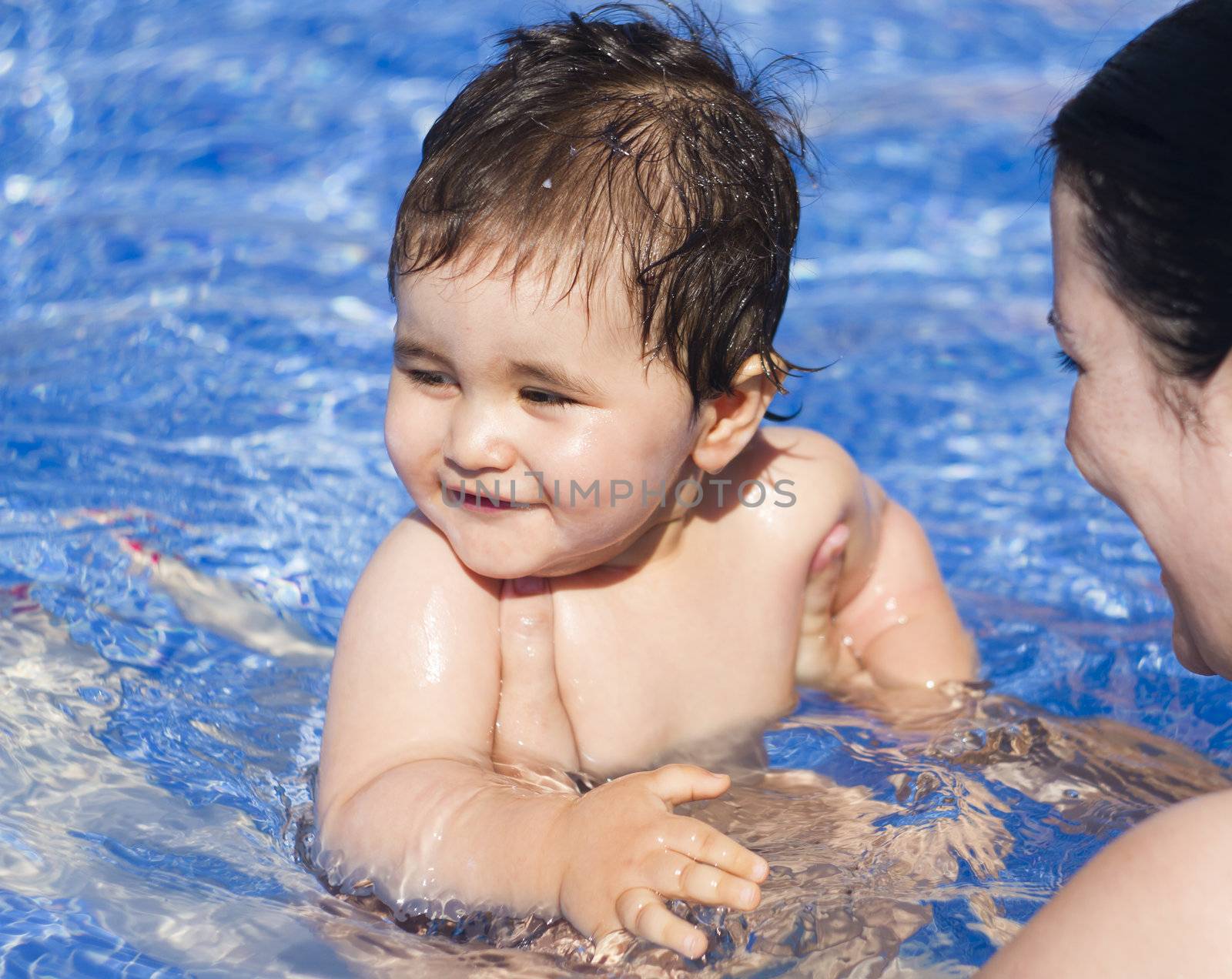 Newborn baby playing in the pool with his mother